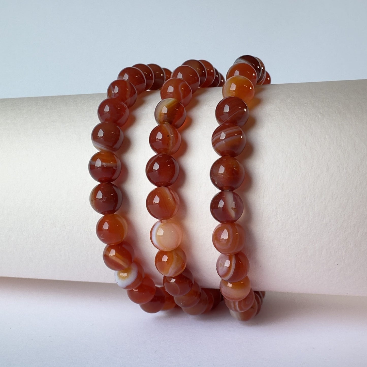 Rød agat armbånd 8mm med glatte perler, snoet elegant omkring en lys cylinder.