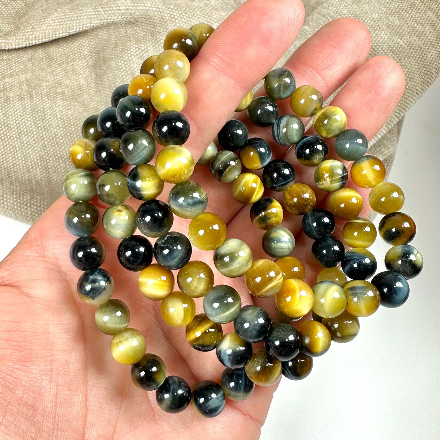 Tiger- og Falkeøje armbånd 8mm i hånd, med skinnende perler i gule og blå nuancer.