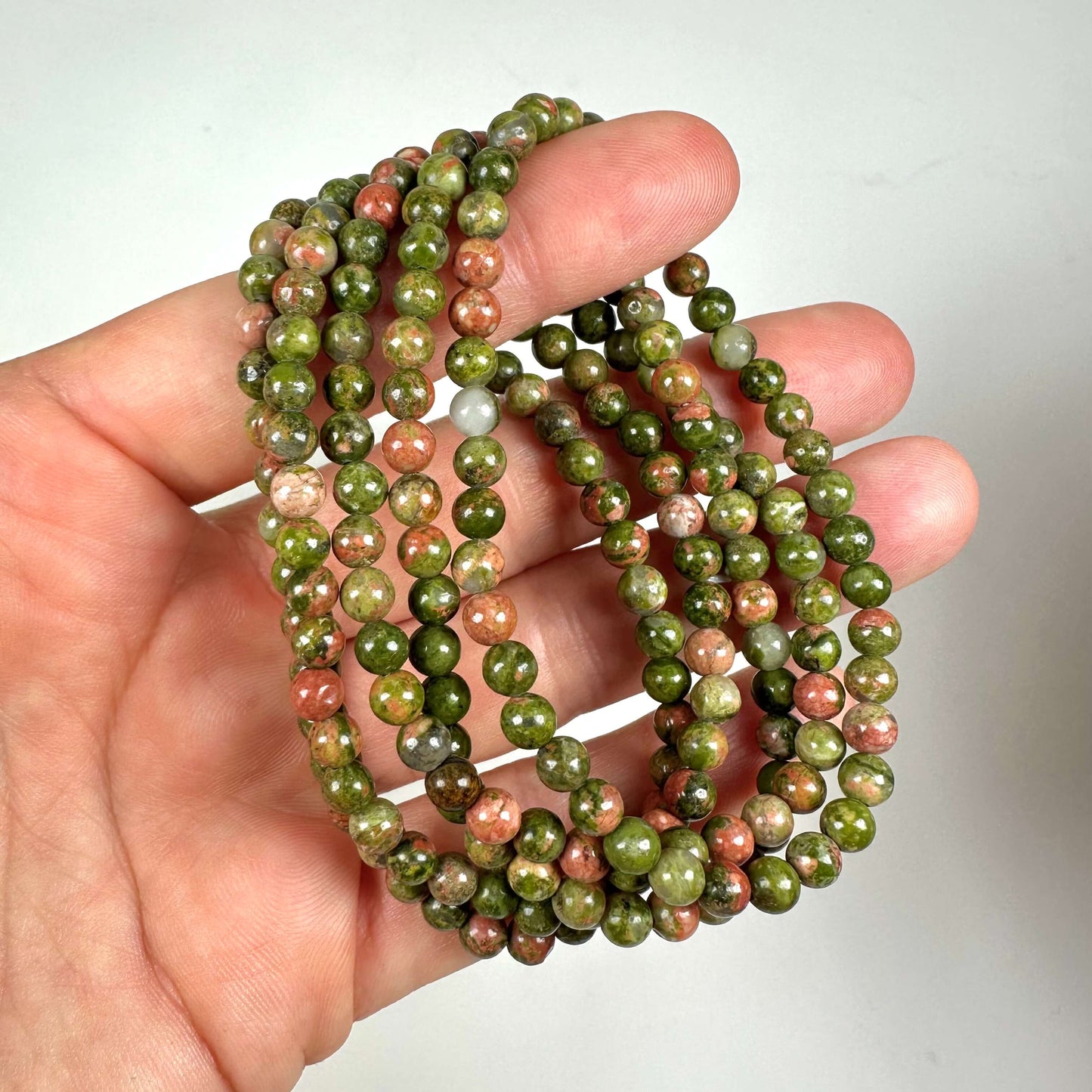 Hånd, der holder et grønligt Unakit armbånd med runde perler i grønne og pink nuancer.
