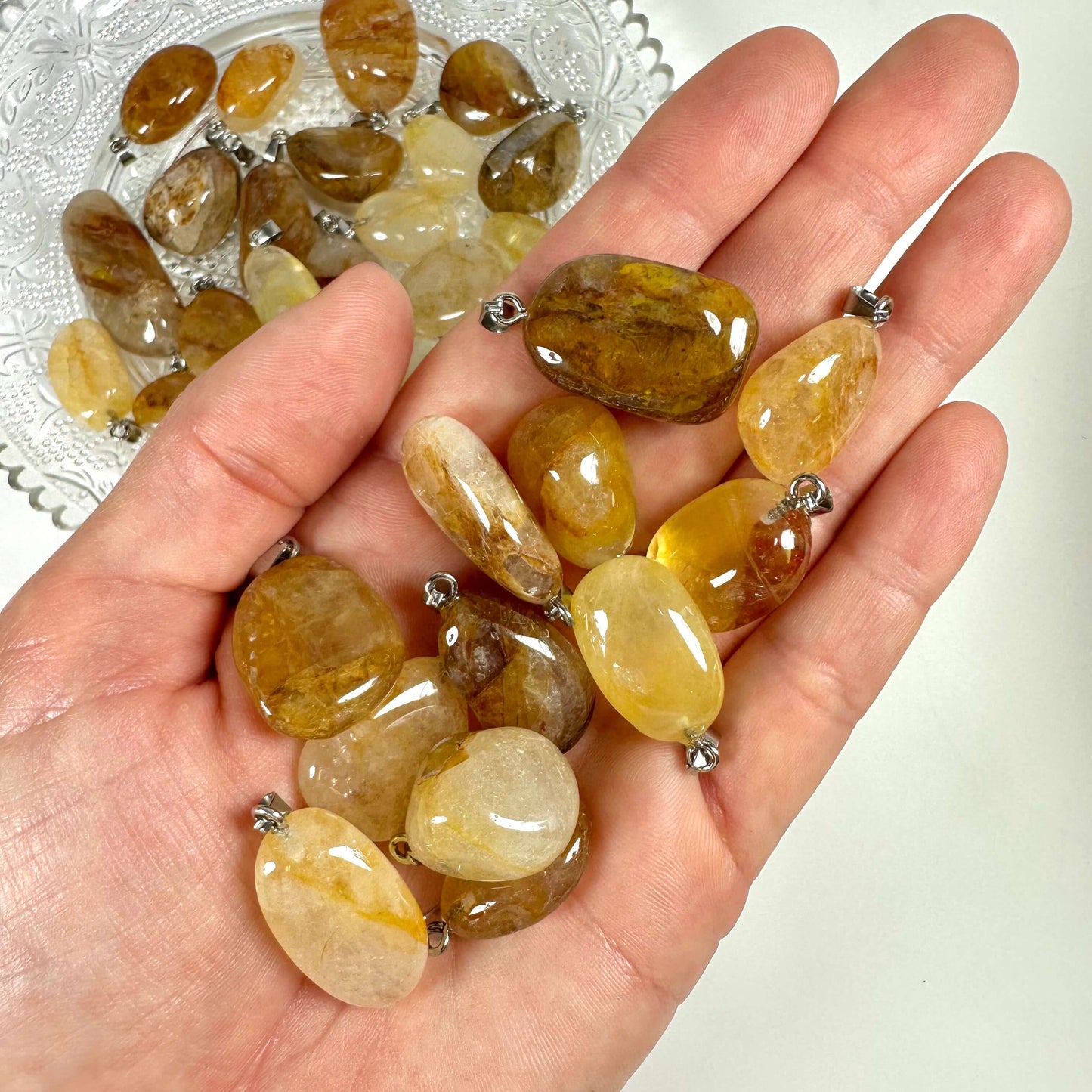 Hånd holder flere Golden healer/hæmatoid vedhæng foran tallerken med lignende sten.