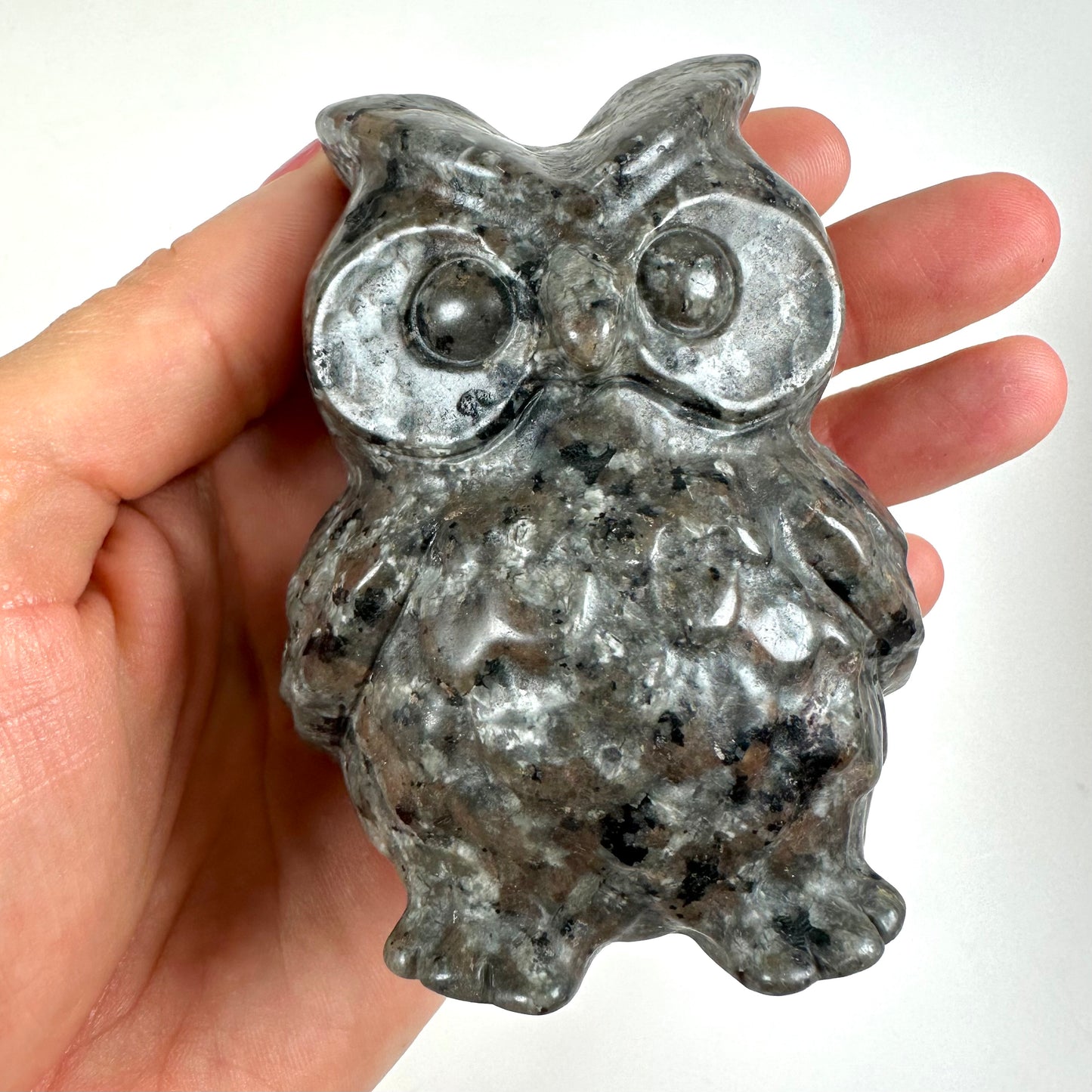 En hånd holder en skulptur af en ugle, lavet af Yooperlit-sten. Uglen har store, runde øjne og detaljeret fjerstruktur.