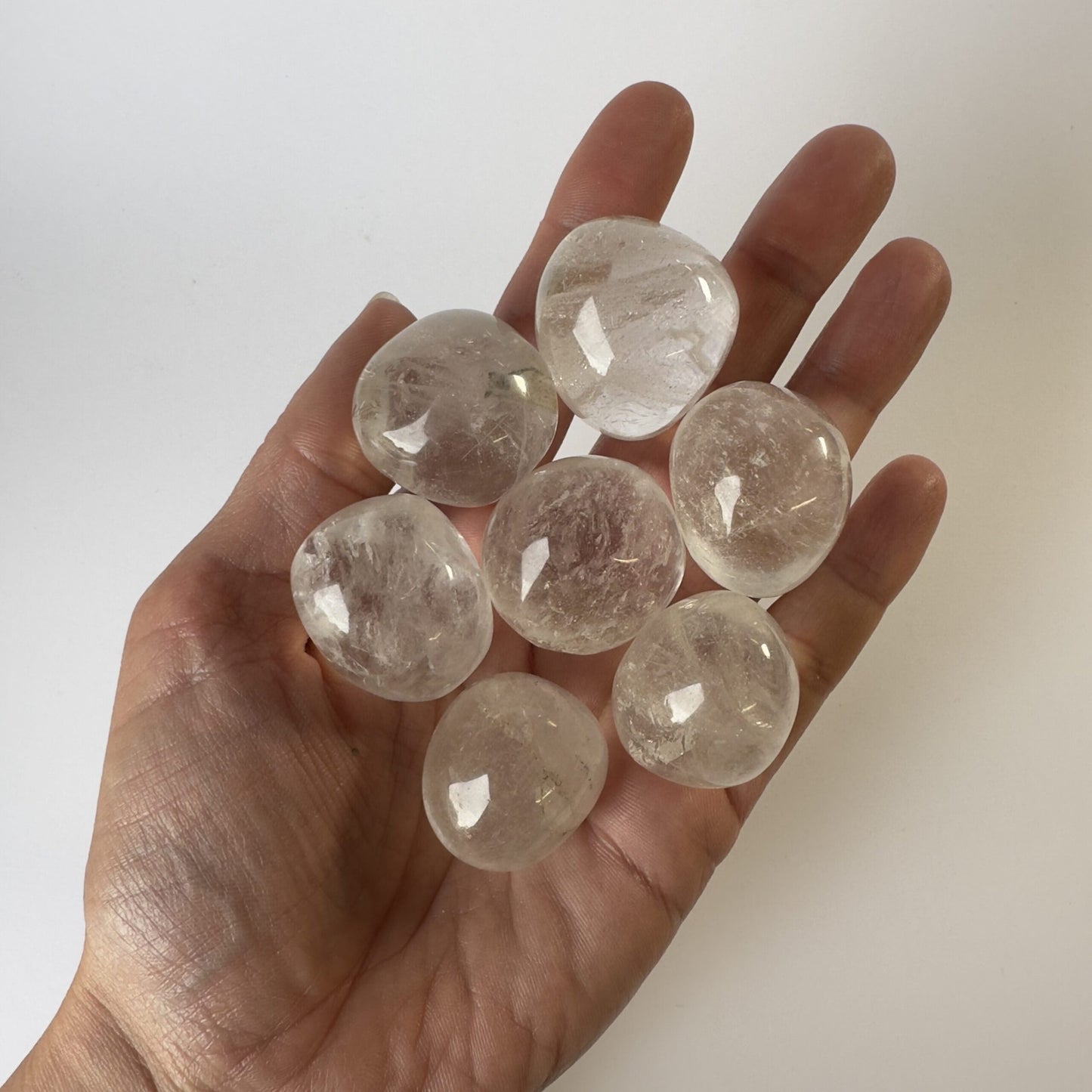 Hånd med syv klare bjergkrystal lommesten mod en hvid baggrund.