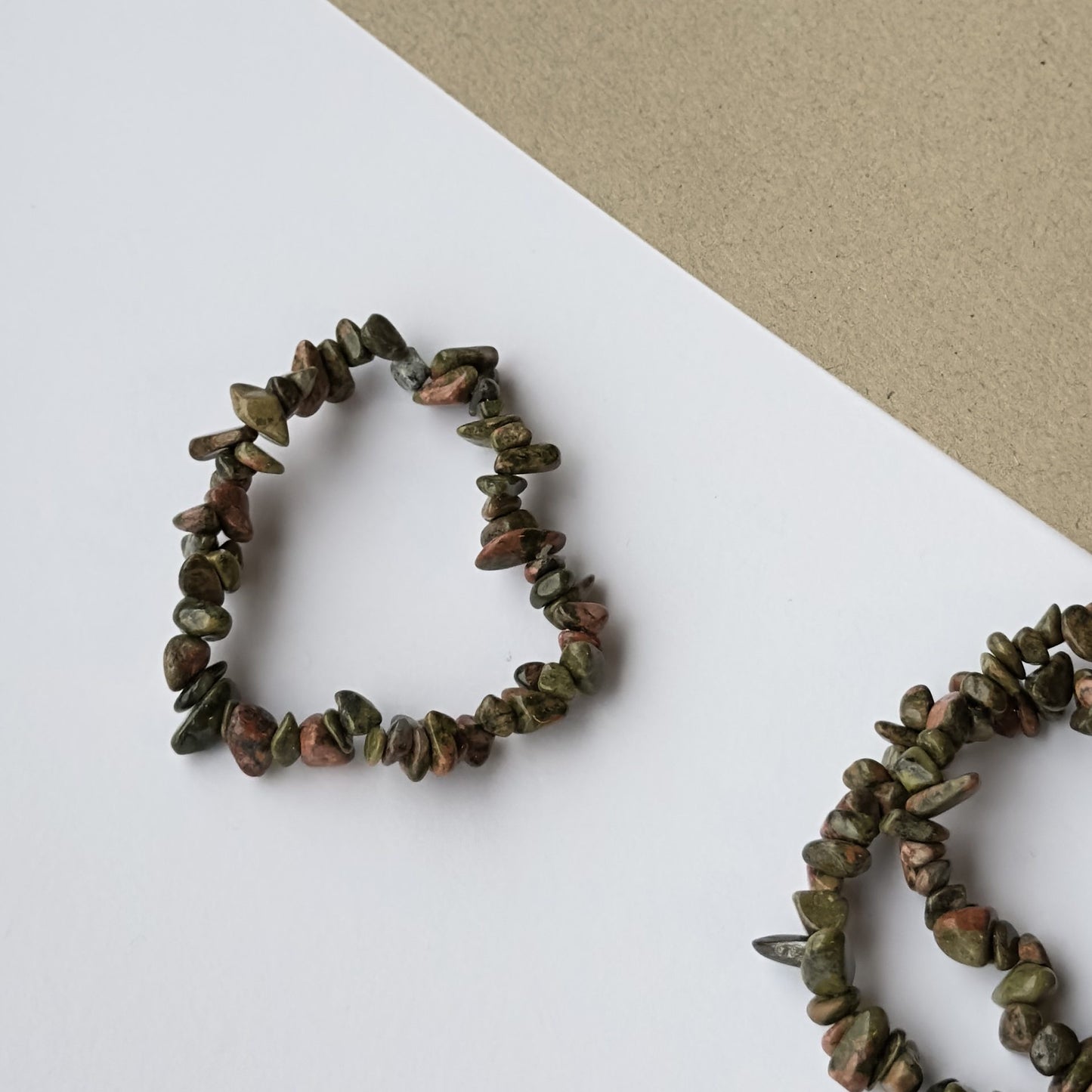 Unakit armbånd formet som hjerte på hvid og grå baggrund.