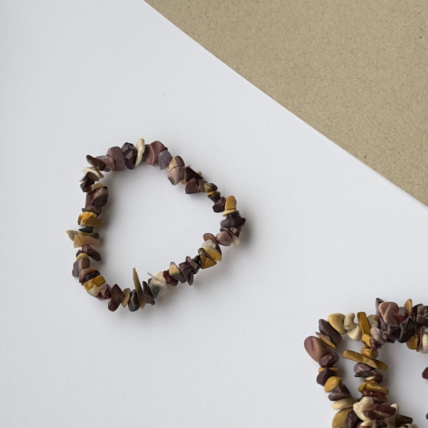 Mookait armbånd lavet af farverige sten på en hvid og brun overflade.