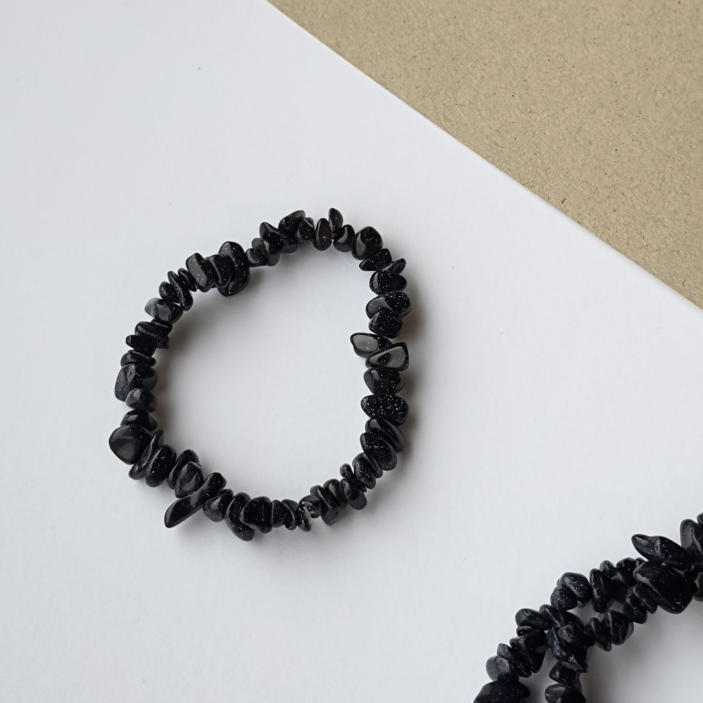 Midnightstone armbånd med sorte perler på hvid og beige baggrund, set oppefra.