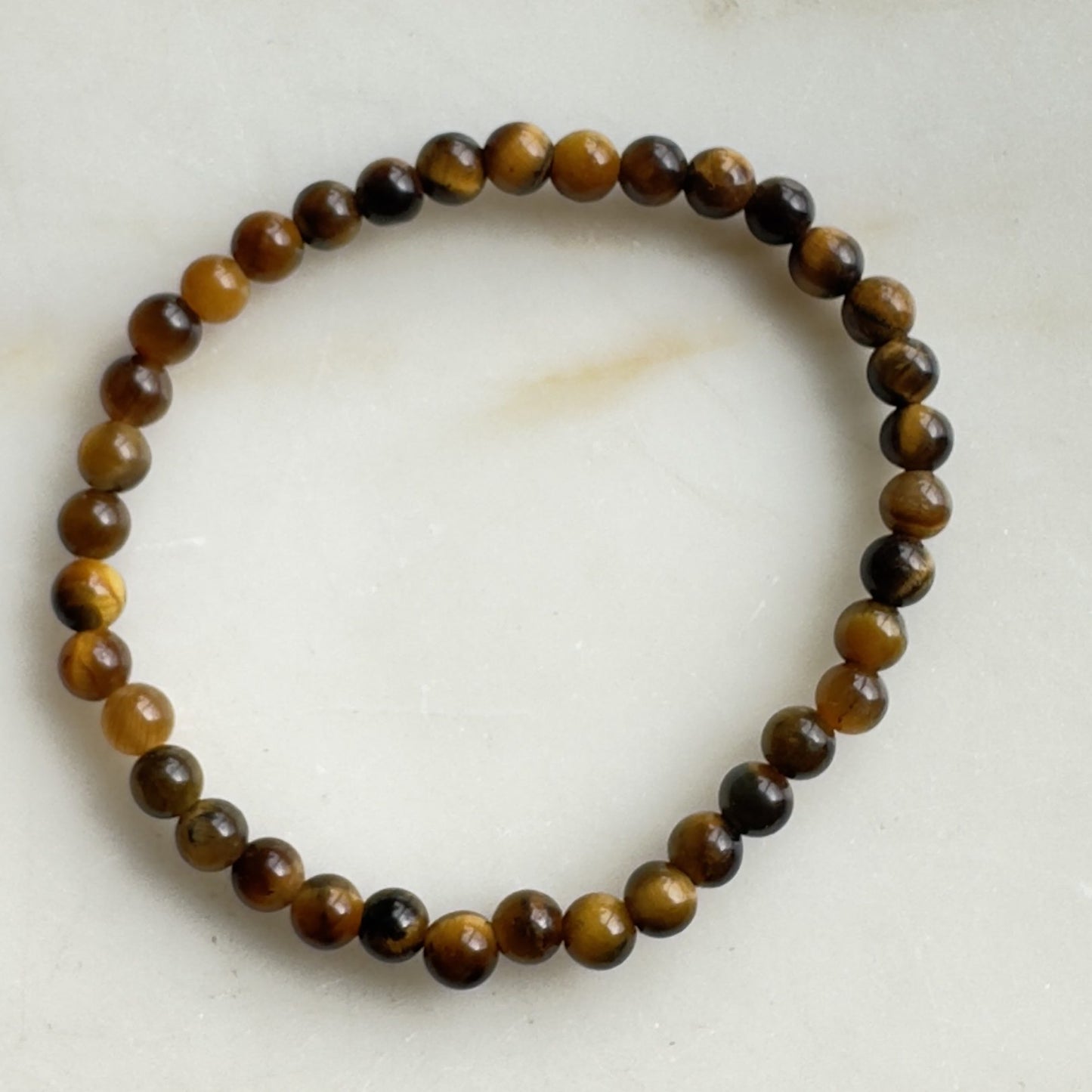 Tigerøje børne armbånd på hvid baggrund med runde perler i gyldne og brune nuancer.