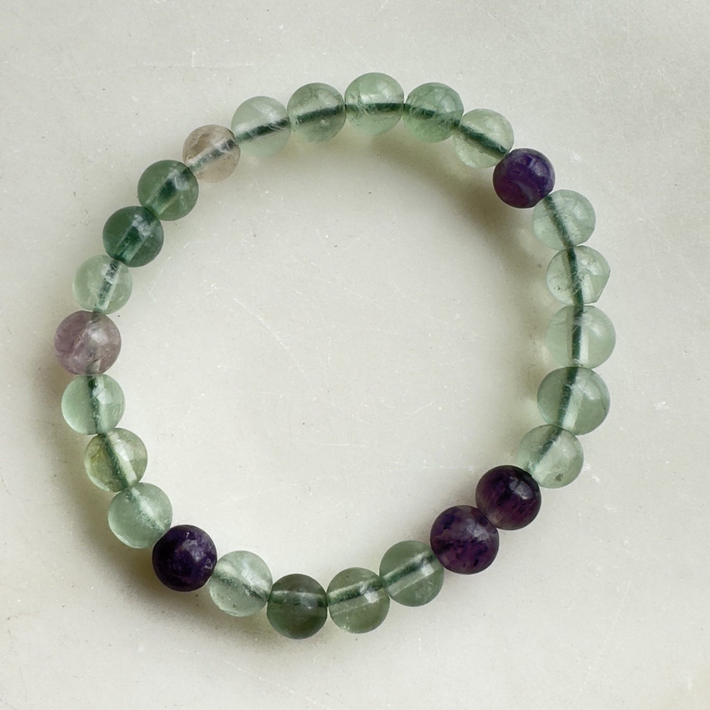 Fluorit børne armbånd med grønne og lilla perler på hvid baggrund.