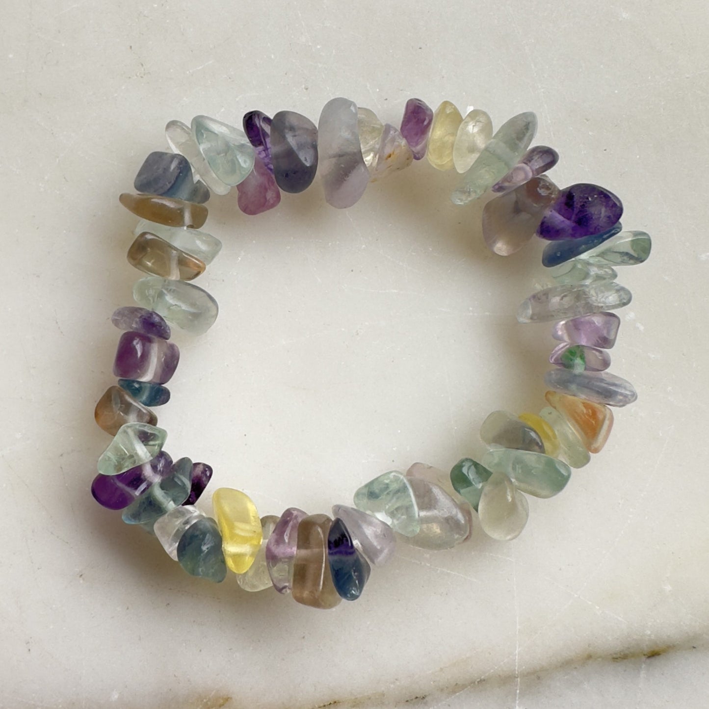 Fluorit børne armbånd med flerfarvede perler i forskellige nuancer på en hvid baggrund.