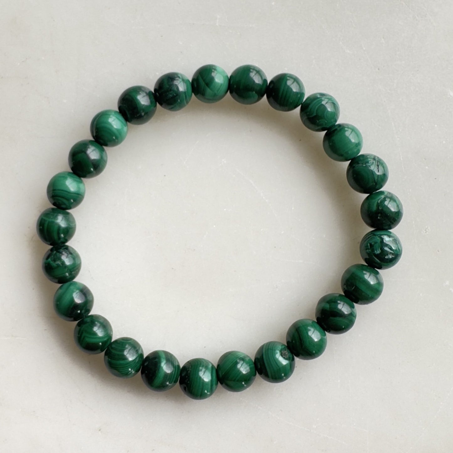 Grønt Malakit børne armbånd med glatte, runde perler arrangeret i en cirkel.