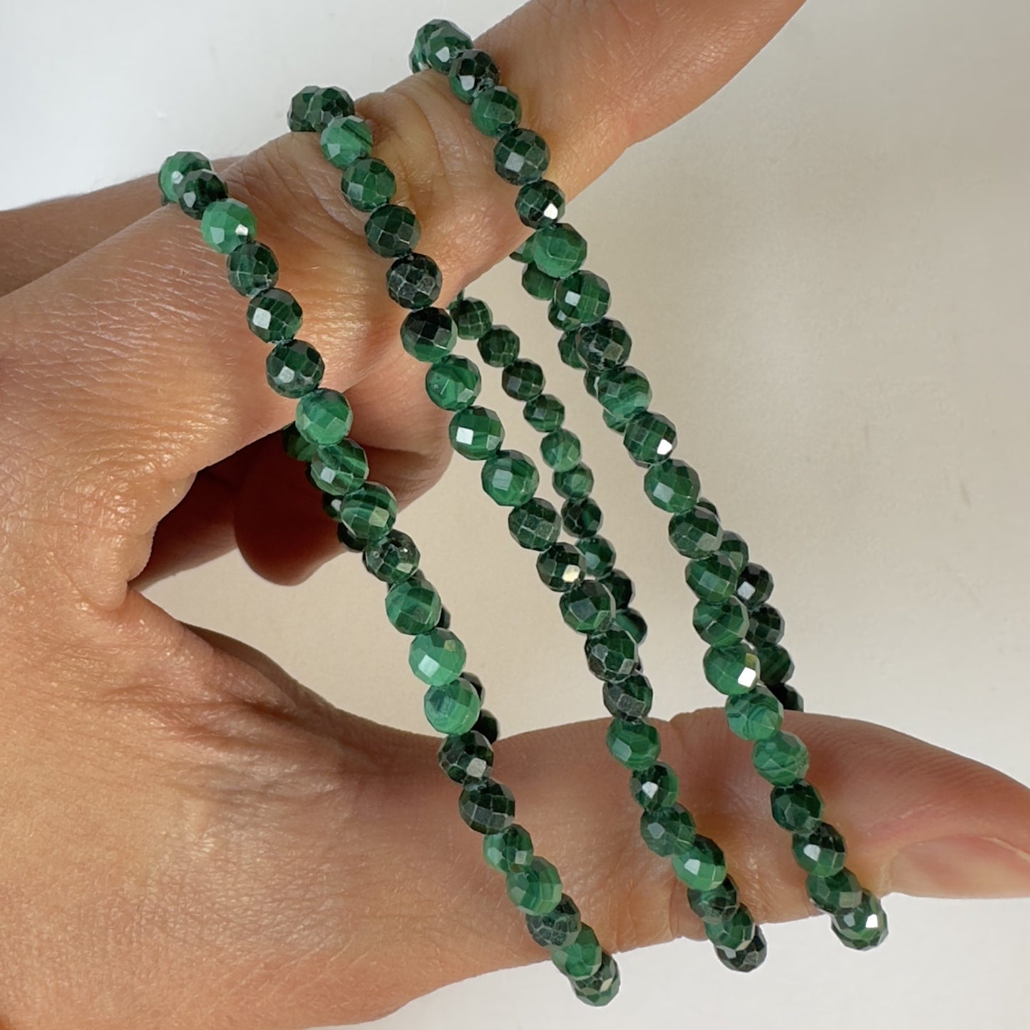 En hånd holder fire facetterede Malakit armbånd i grønne nuancer.