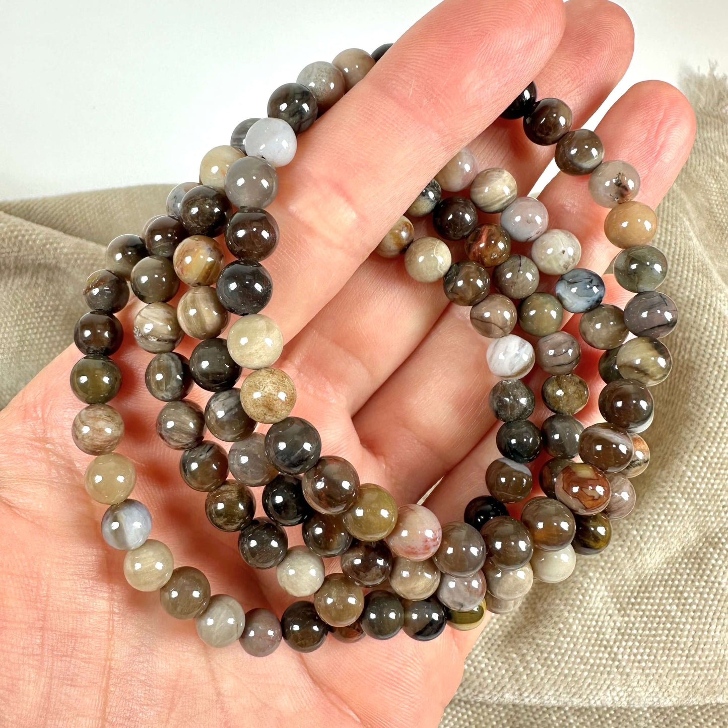 En hånd holder en række farverige perler i naturlige jordfarver, mod en neutral baggrund.