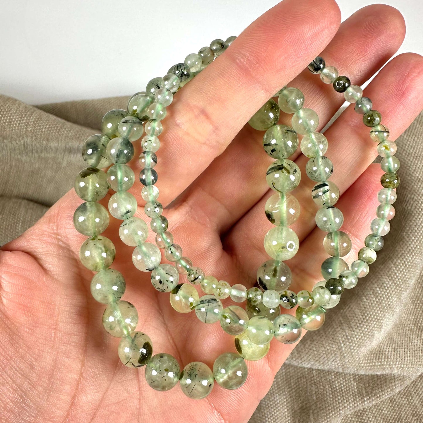 Grønne perlearmbånd holdt i en hånd over en brun baggrund.