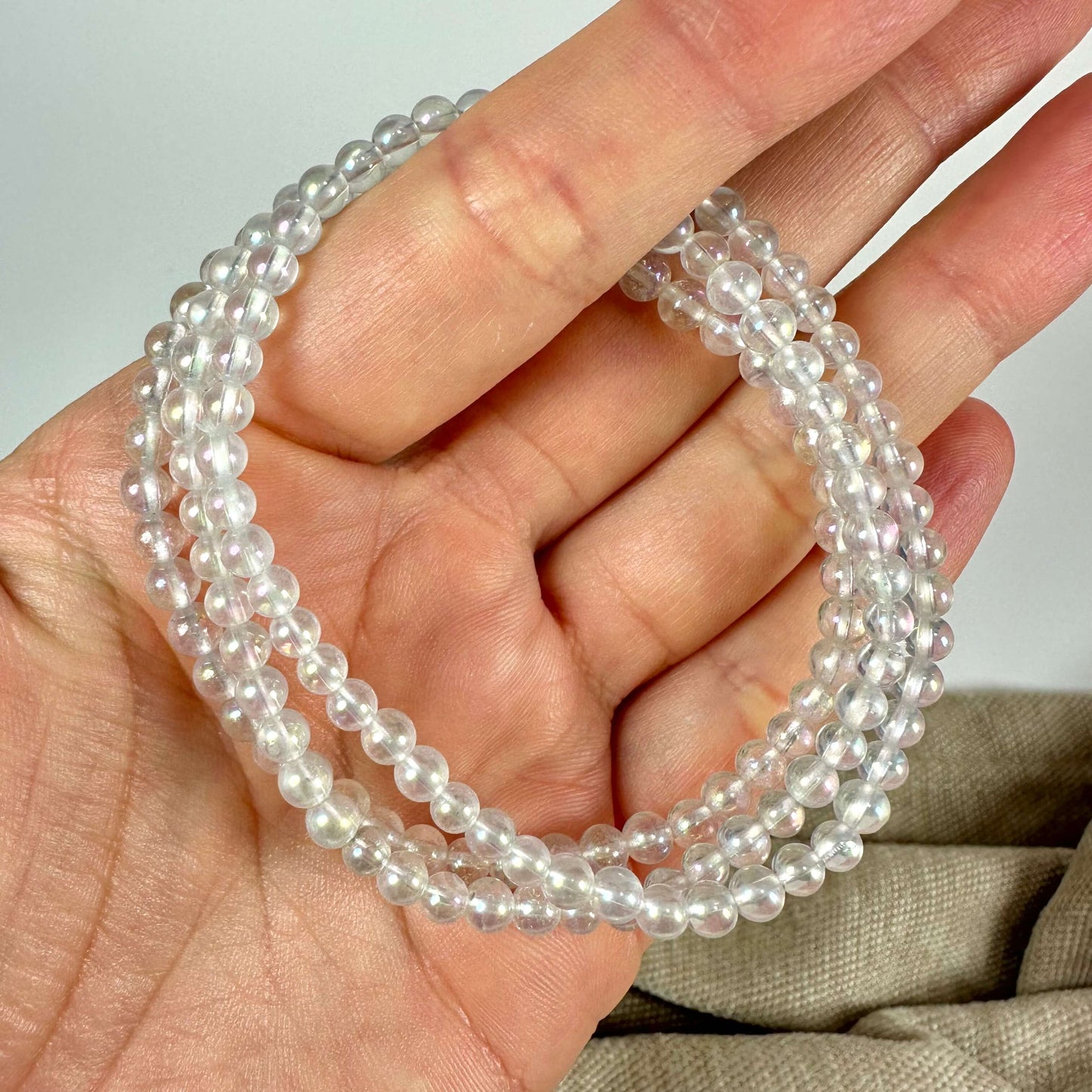 Hånd holder gennemsigtige perlekæder mod en lys baggrund.