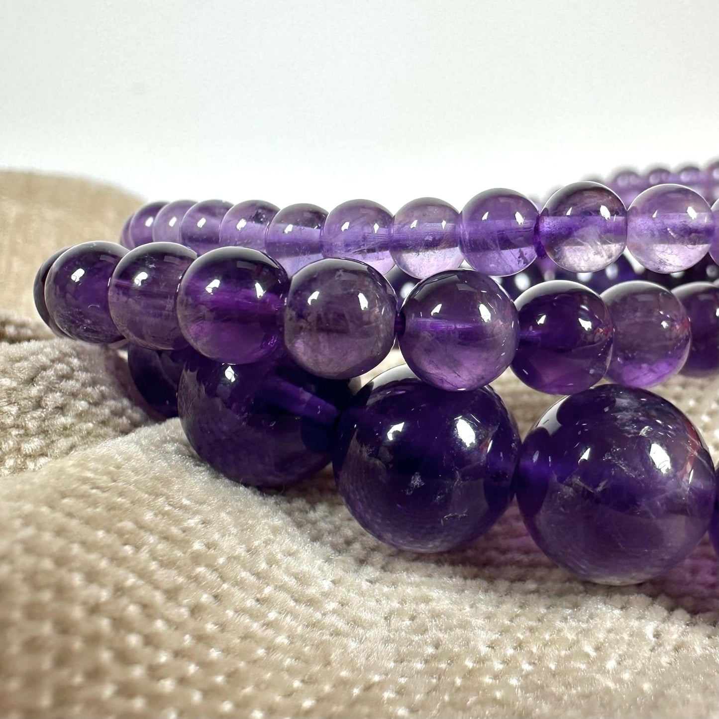 En række af lilla glasperler ligger på en beige tekstilbaggrund.