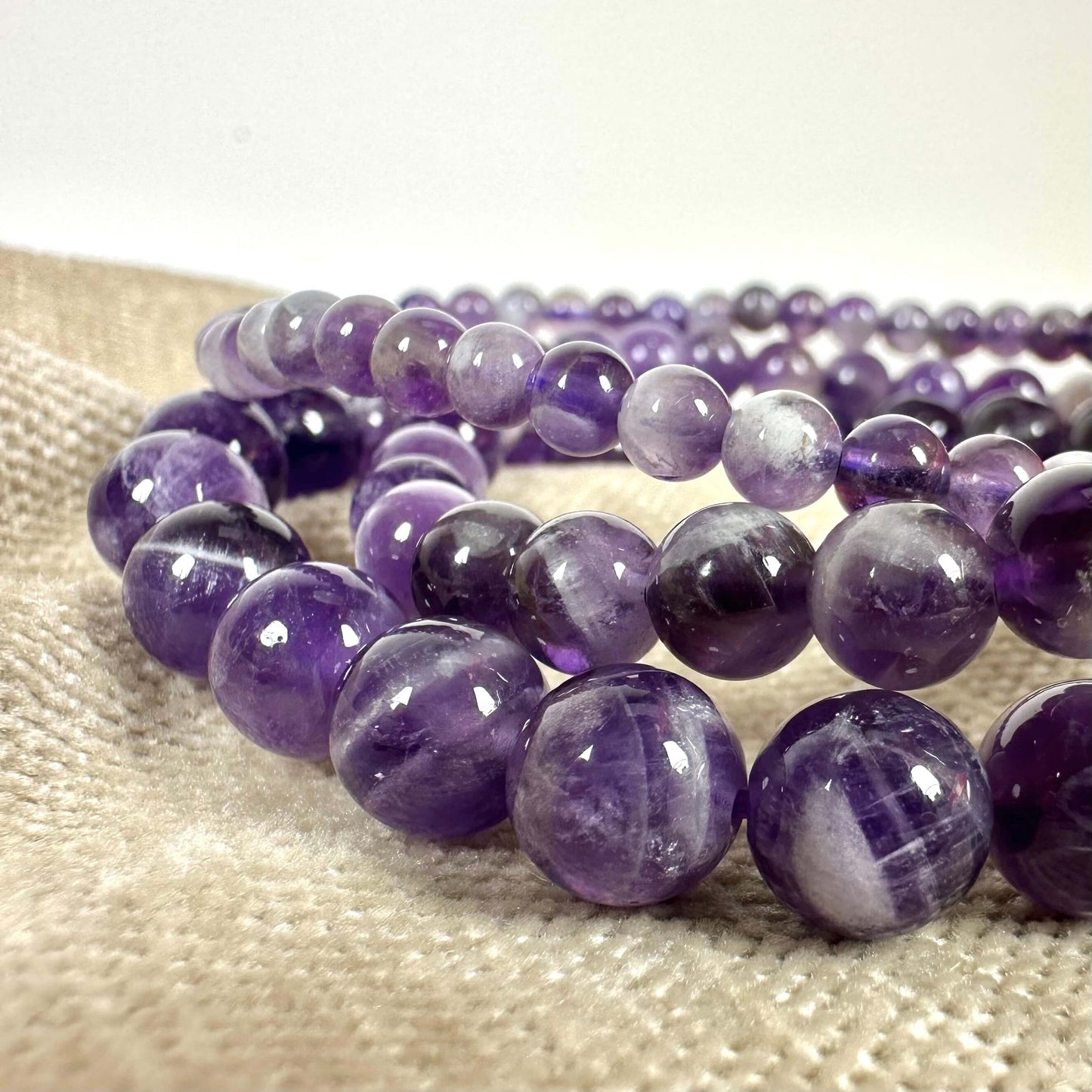 Lilla ametystperler på beige stof, fremhæver deres glans og naturlige skønhed i lyset.