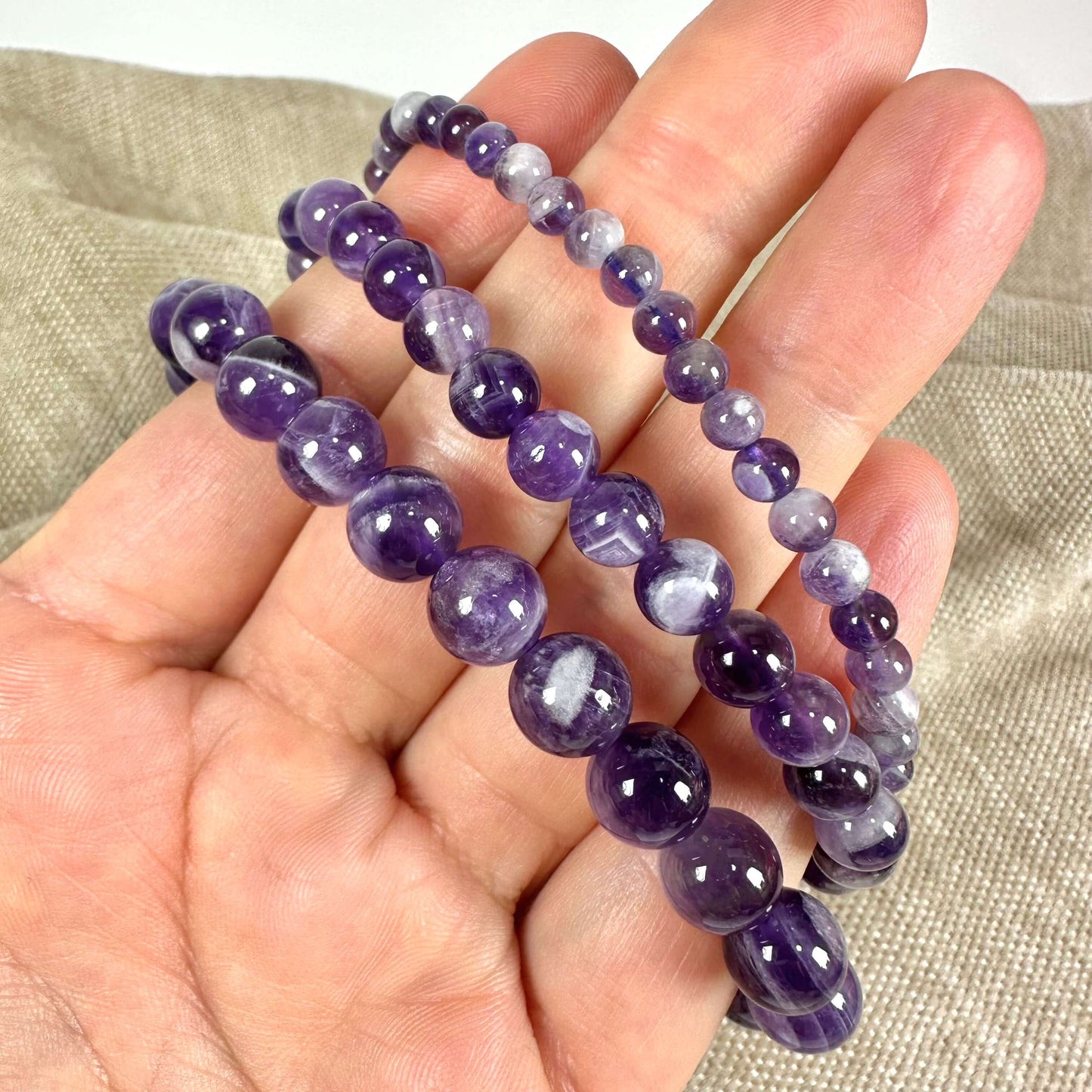 Armbånd med lilla ametystperler i forskellige størrelser holdes i en hånd.
