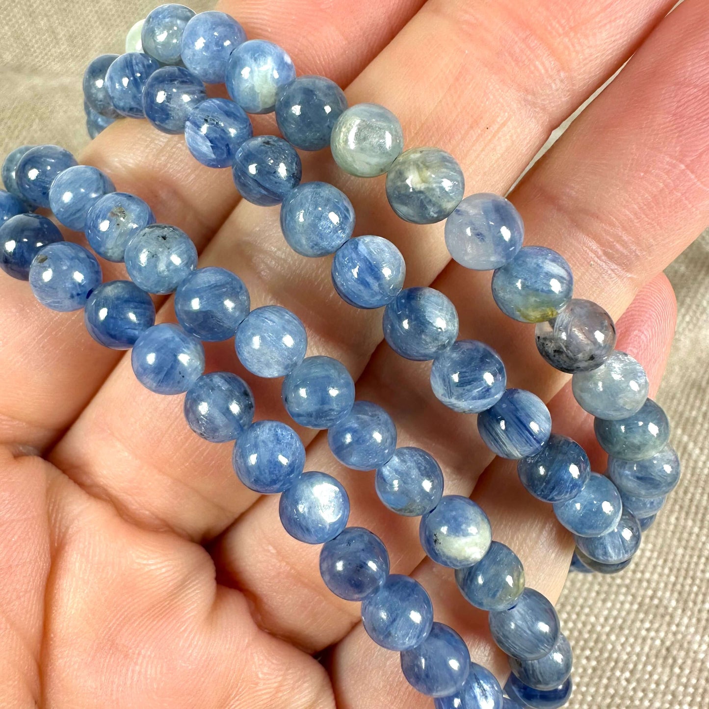 Armbånd med blå perler holdes i hånd, viser lyse og mørke blå nuancer på beige baggrund.