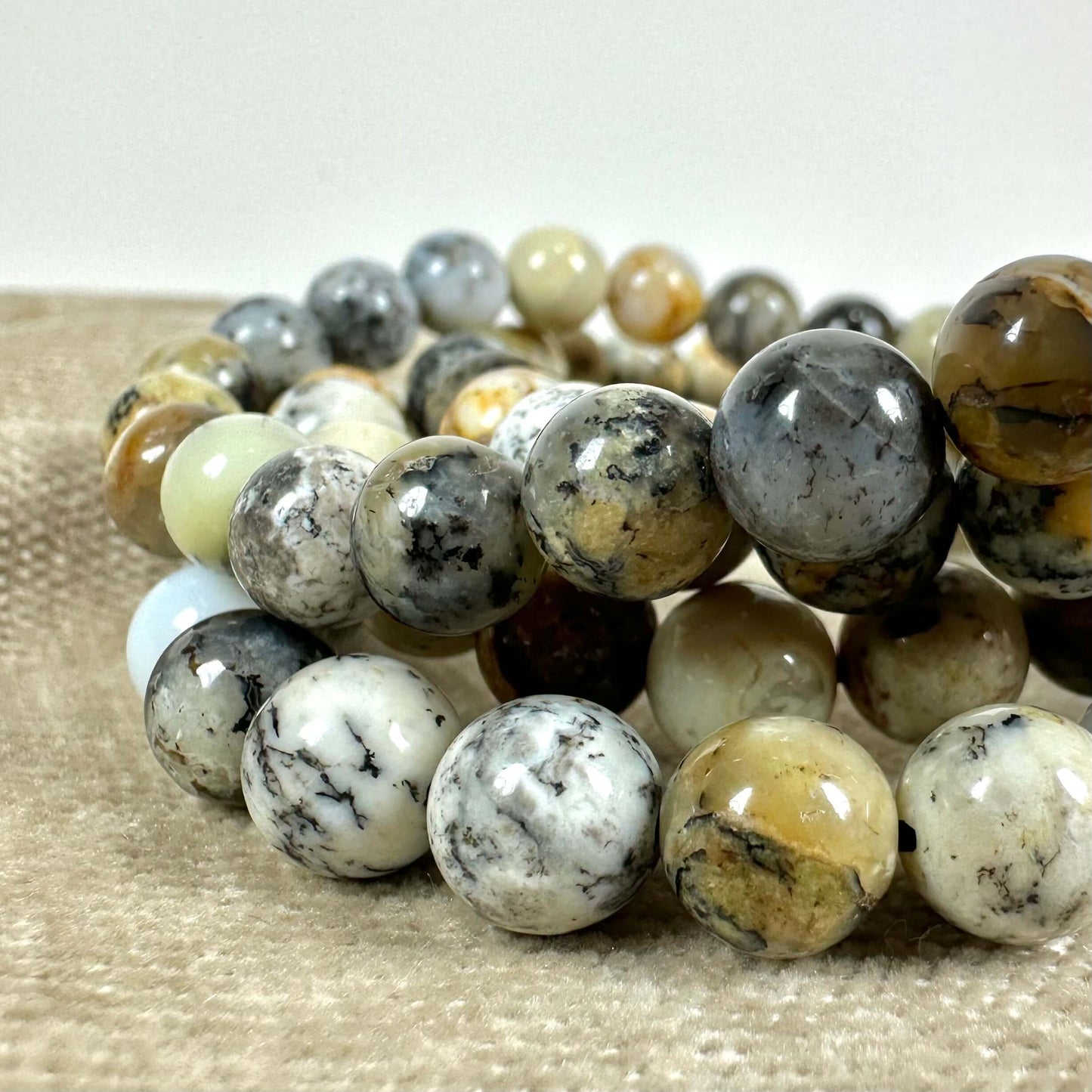 Armbånd med polerede, flerfarvede natursten i nærbillede på en beige overflade.