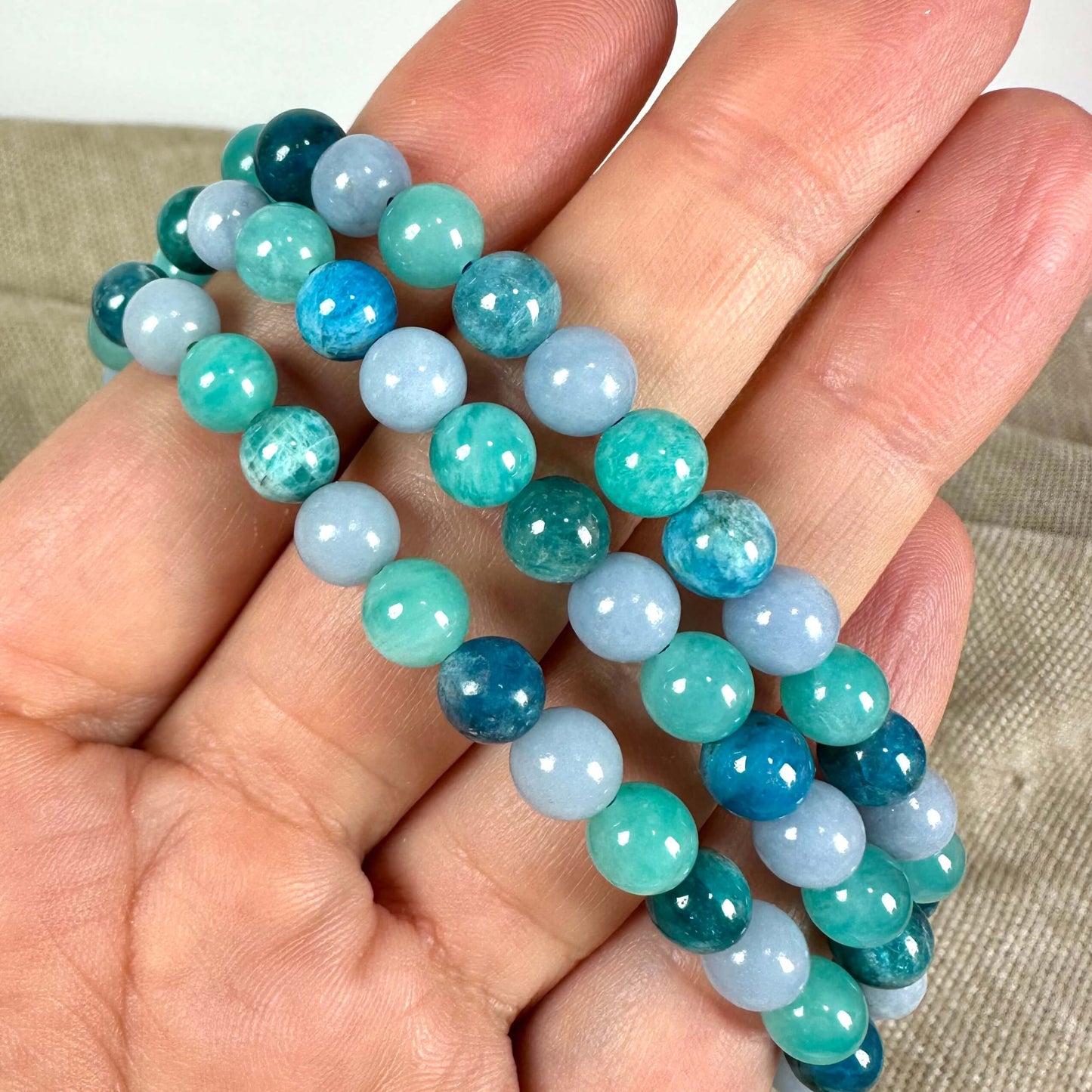 Armbånd med flerfarvede perler i blå og grønne nuancer holdes i en hånd.