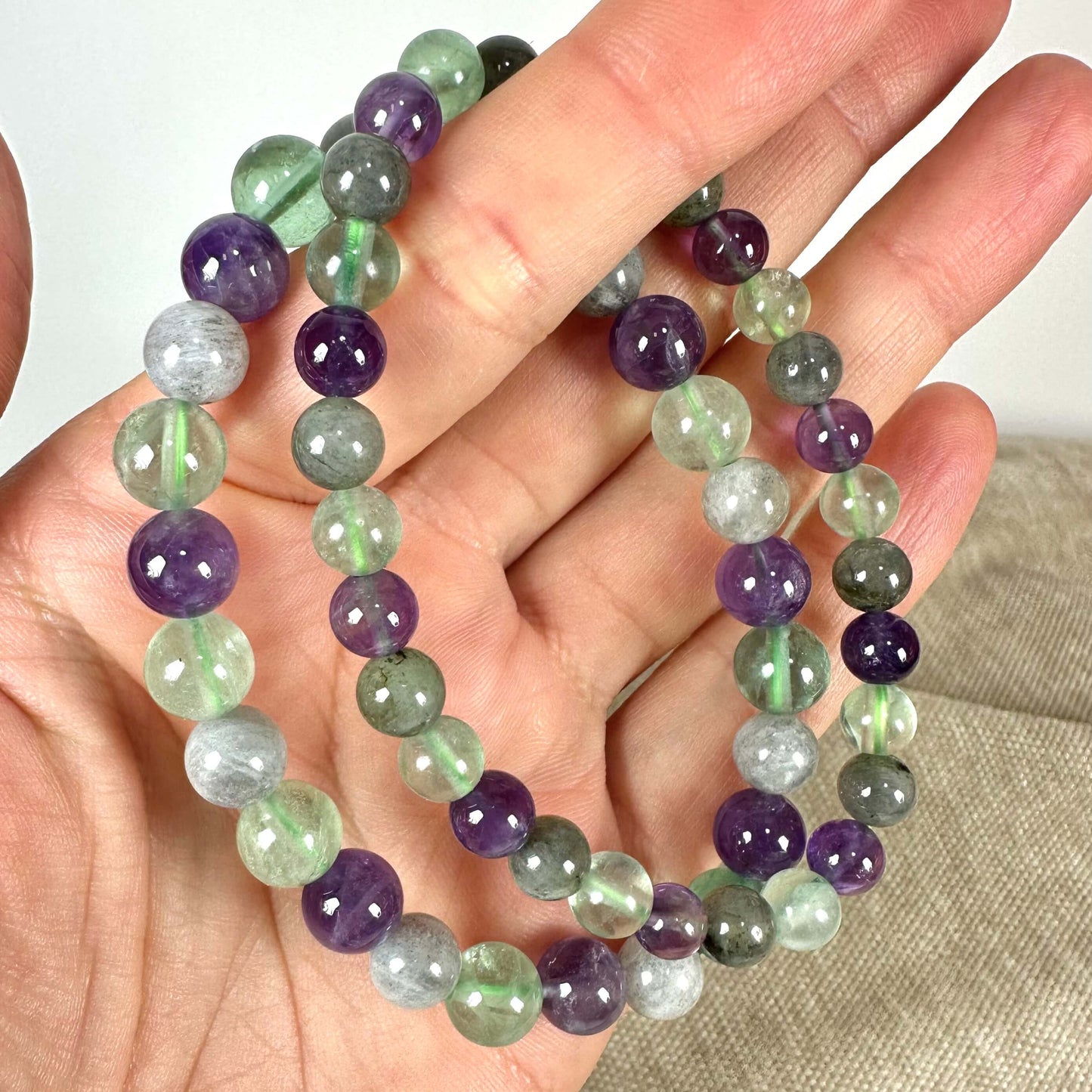 En hånd holder en flerfarvet perlekæde med grønne, lilla og grå perler.
