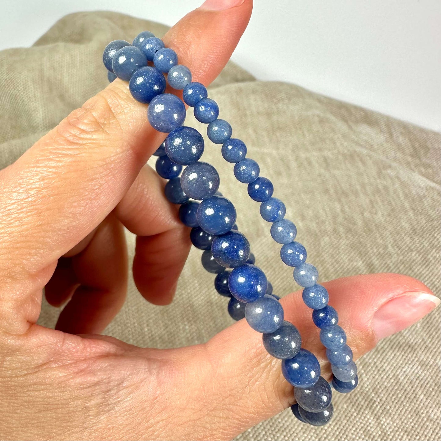 En hånd holder to blå perlearmbånd mod en lys beige baggrund.