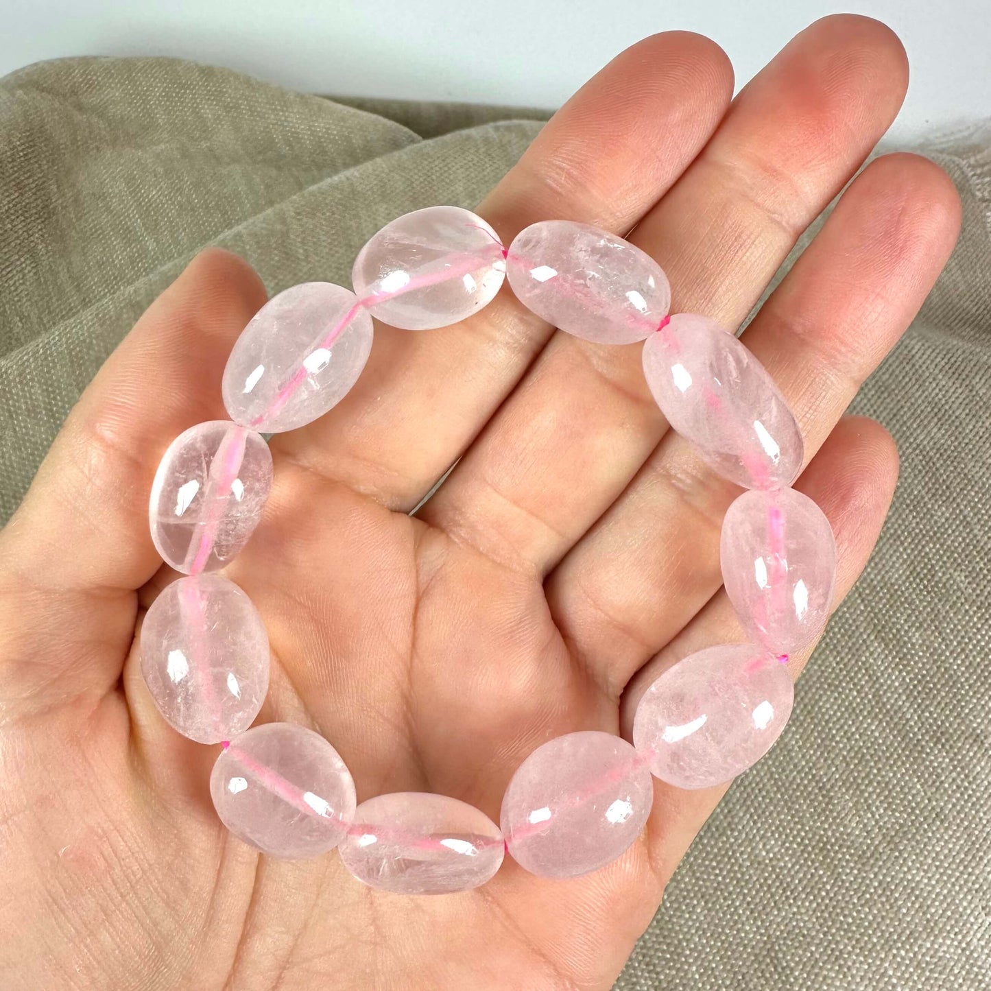 Armbånd med lyserøde sten placeret i en åben håndflade på en lys baggrund.