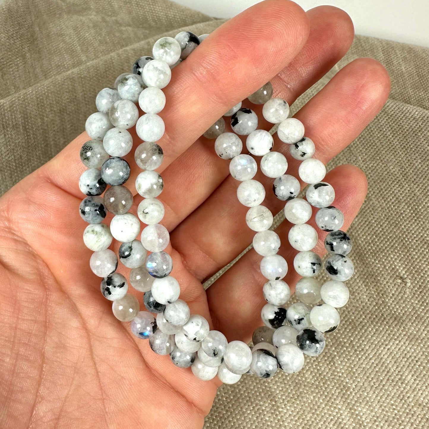 En hånd holder en halskæde af hvide og sorte perler på en beige baggrund.