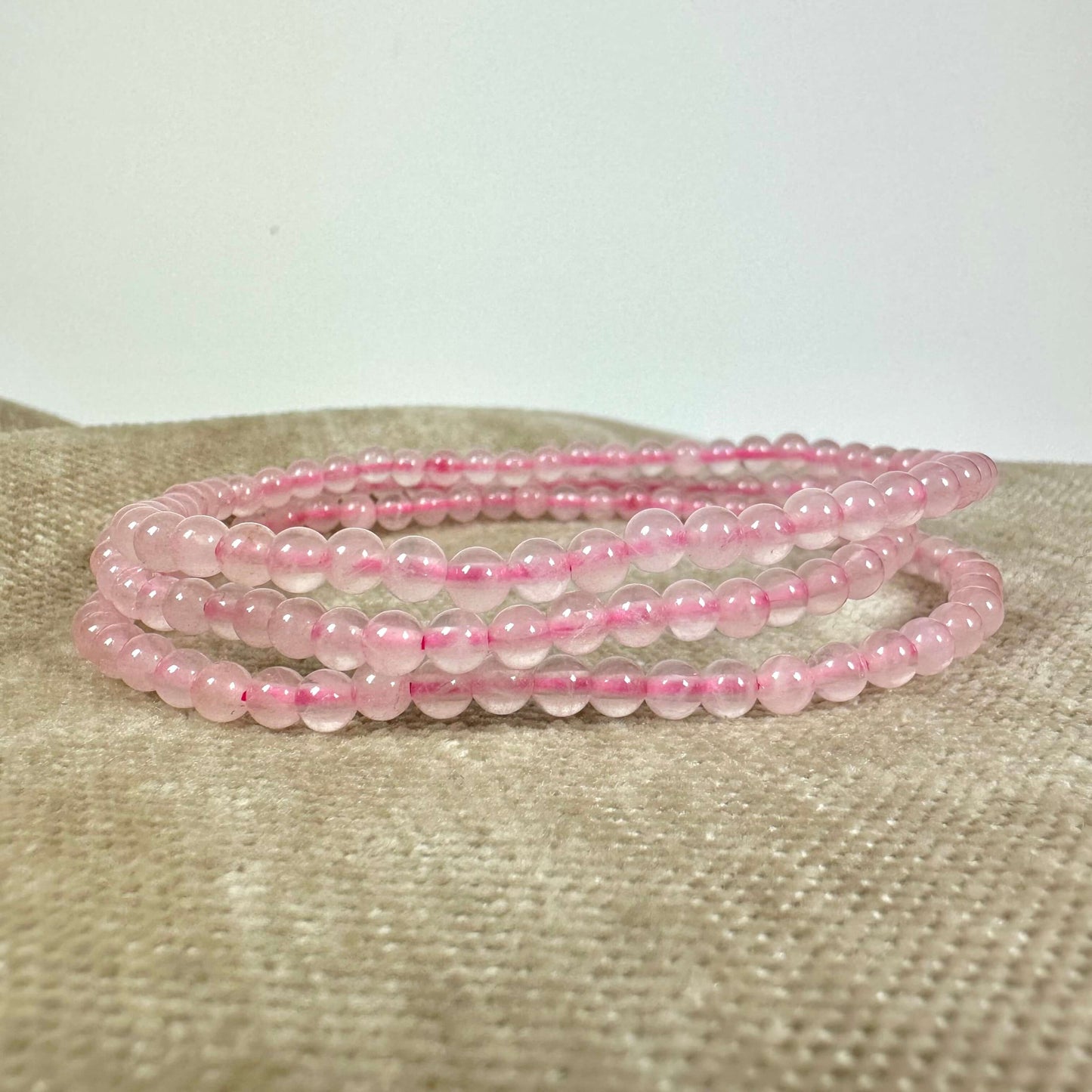 Lyserøde perlearmbånd lagt i en spiral på en beige overflade.
