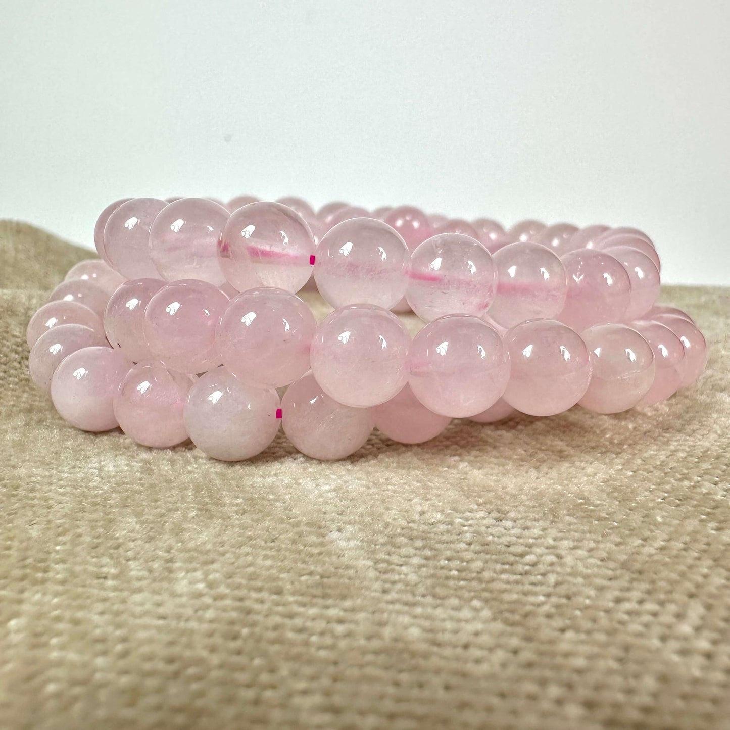 Armbånd med lyserøde kugler ligger på en lys beige stofbaggrund.