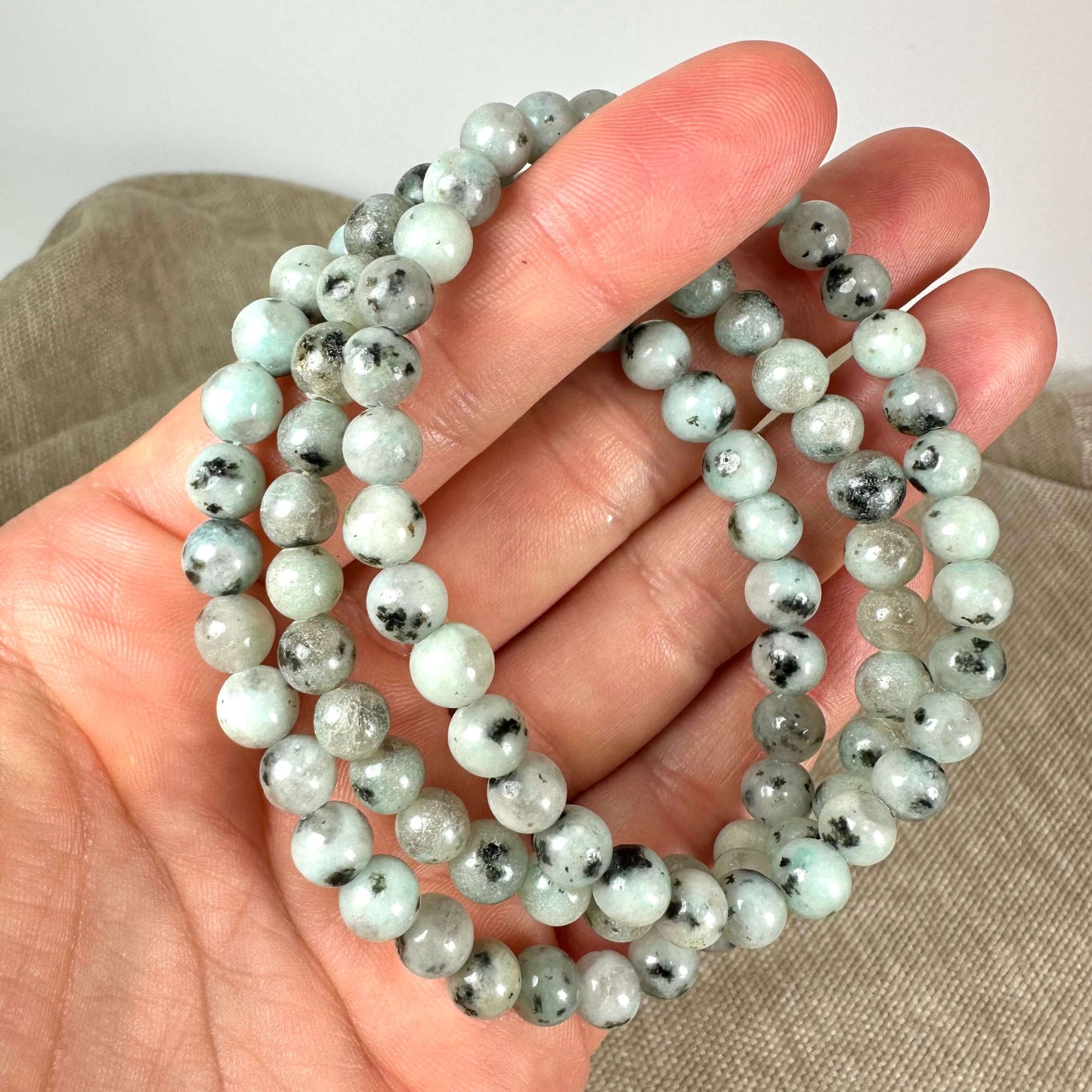 En hånd holder en snor med grønne og sorte marmorerede perler tæt op af brun baggrund.