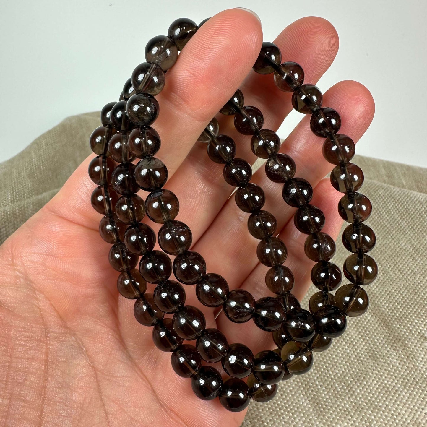 En hånd holder en lang kæde af blanke, mørkebrune perler. Baggrunden er en lys stofoverflade.
