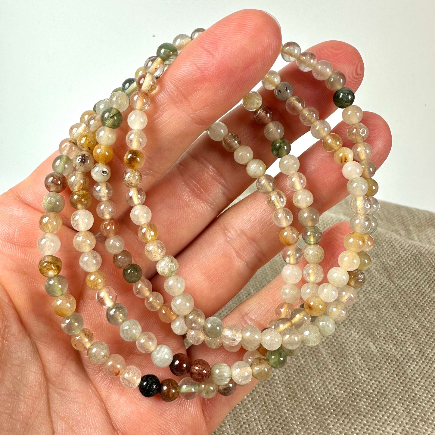 En hånd holder smykker af flerfarvede perler på en neutral baggrund.