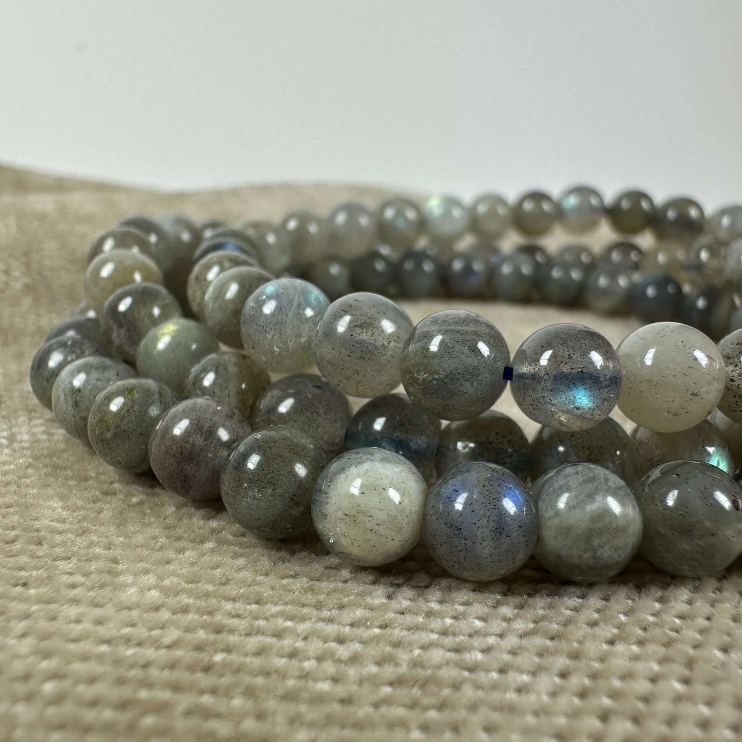 Grå labradoritperler med blålige nuancer, arrangeret på en beige overflade.
