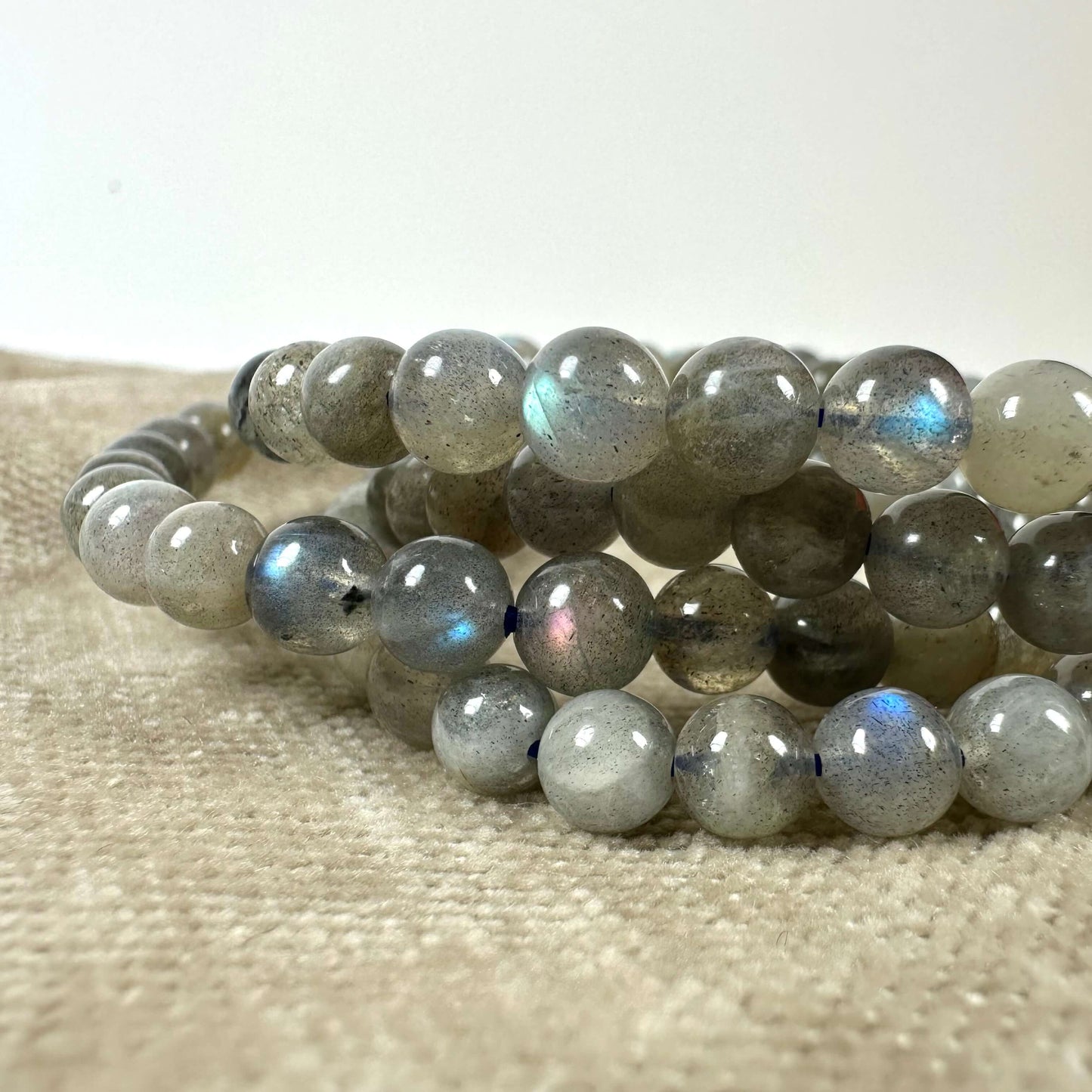 Armbånd af labradoritkrystaller ligger på beige stof, viser iriserende skær.