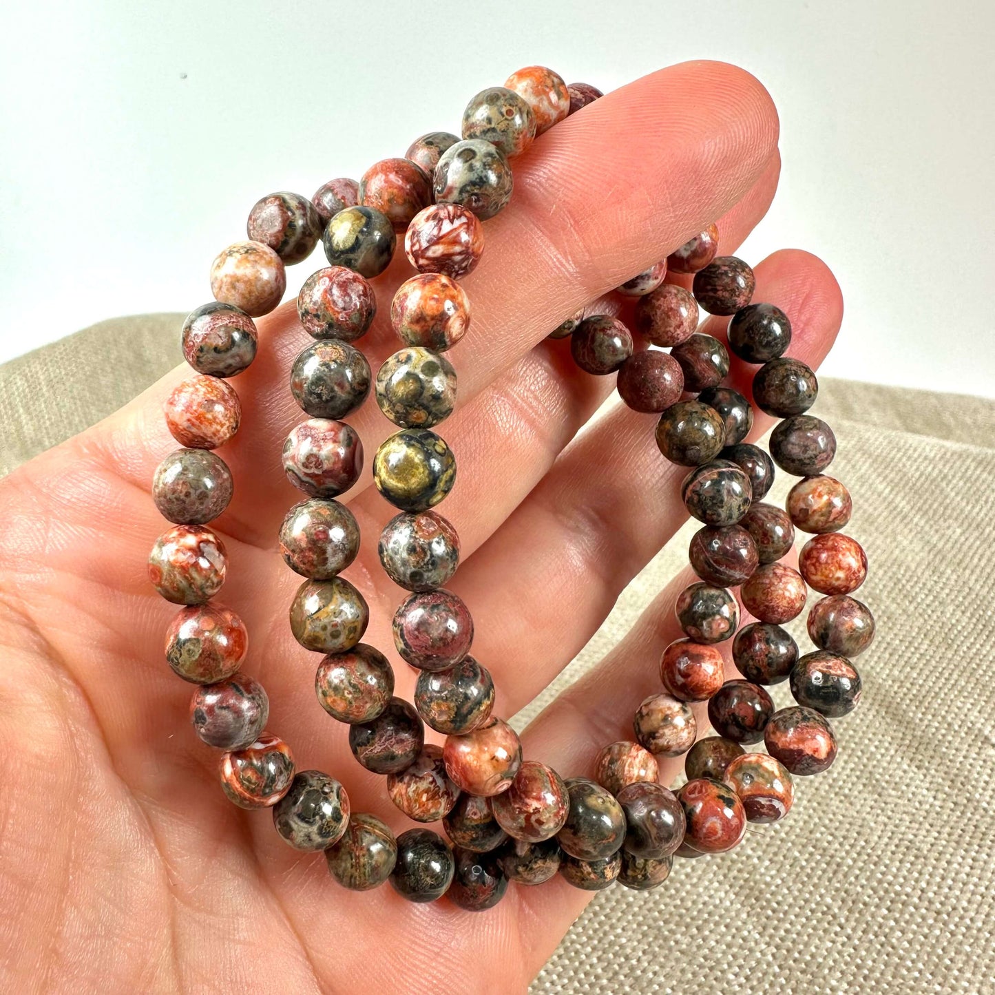 Perlehalskæde i jordfarver holdt i en hånd på en beigefarvet baggrund.