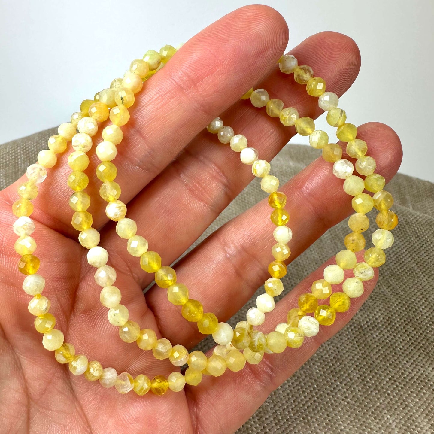En hånd holder en gul perlehalskæde med små, facetterede perler.