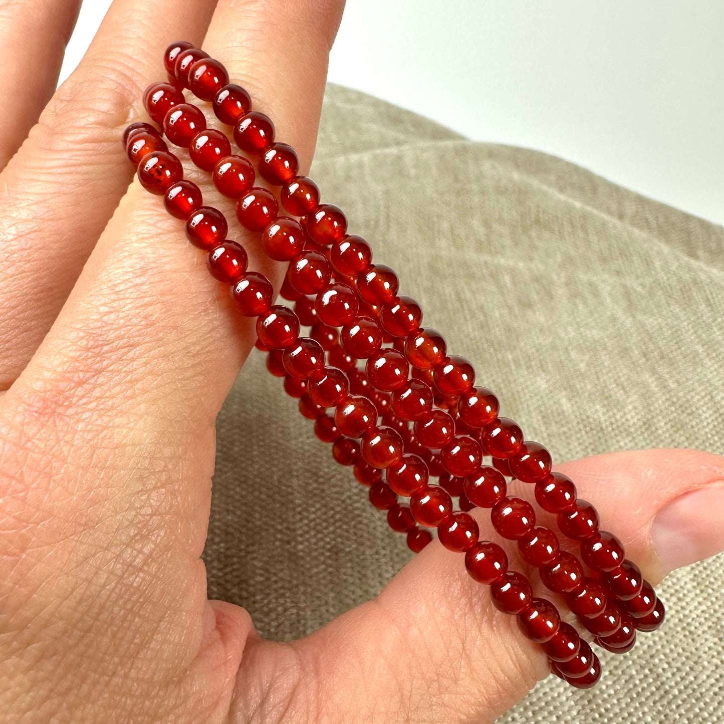 En hånd holder fire røde perlearmbånd mod en neutral baggrund.