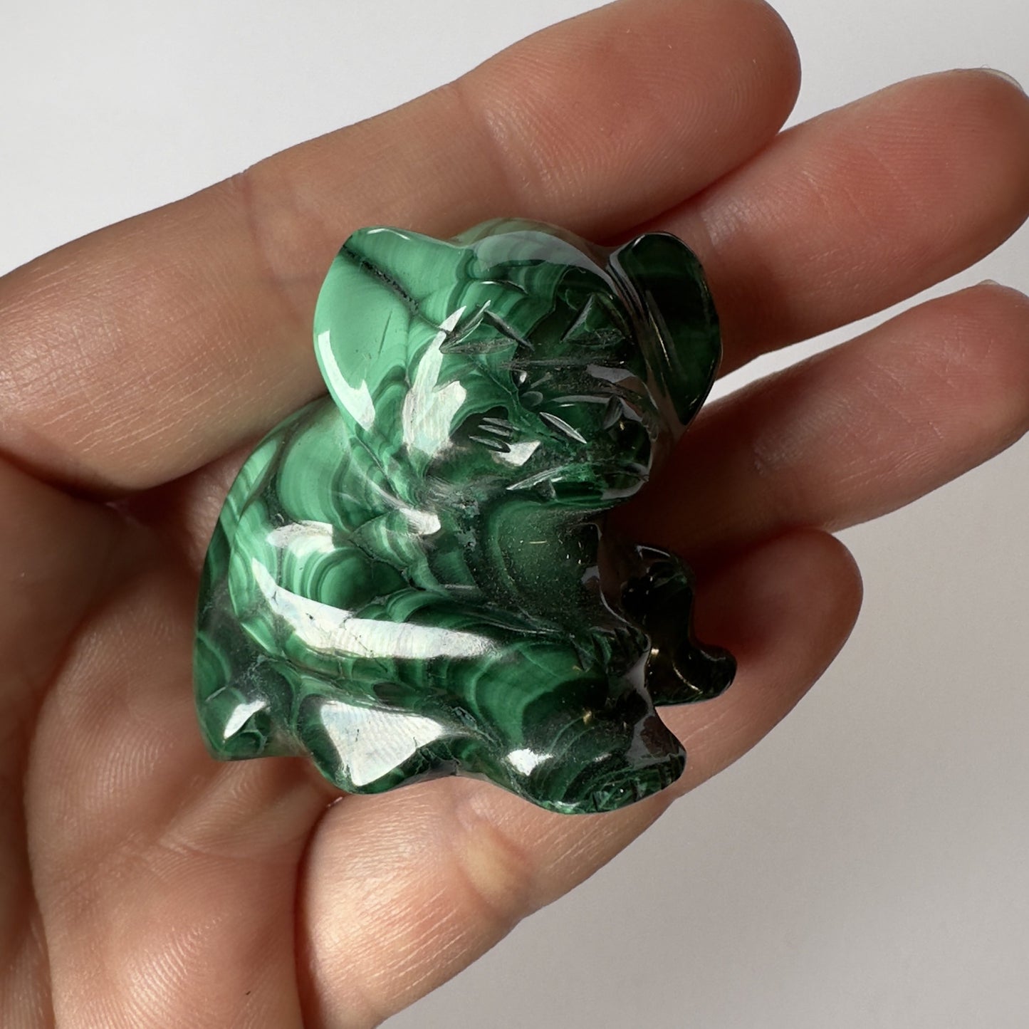 En hånd holder en lille skulptur af en malakit abe med skinnende, grønne striber.