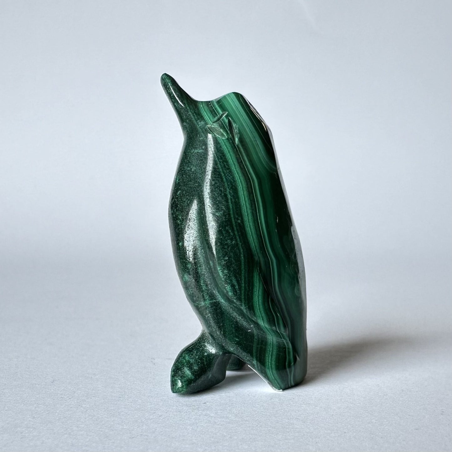 Malakit pingvin figur står oprejst på en lys baggrund.