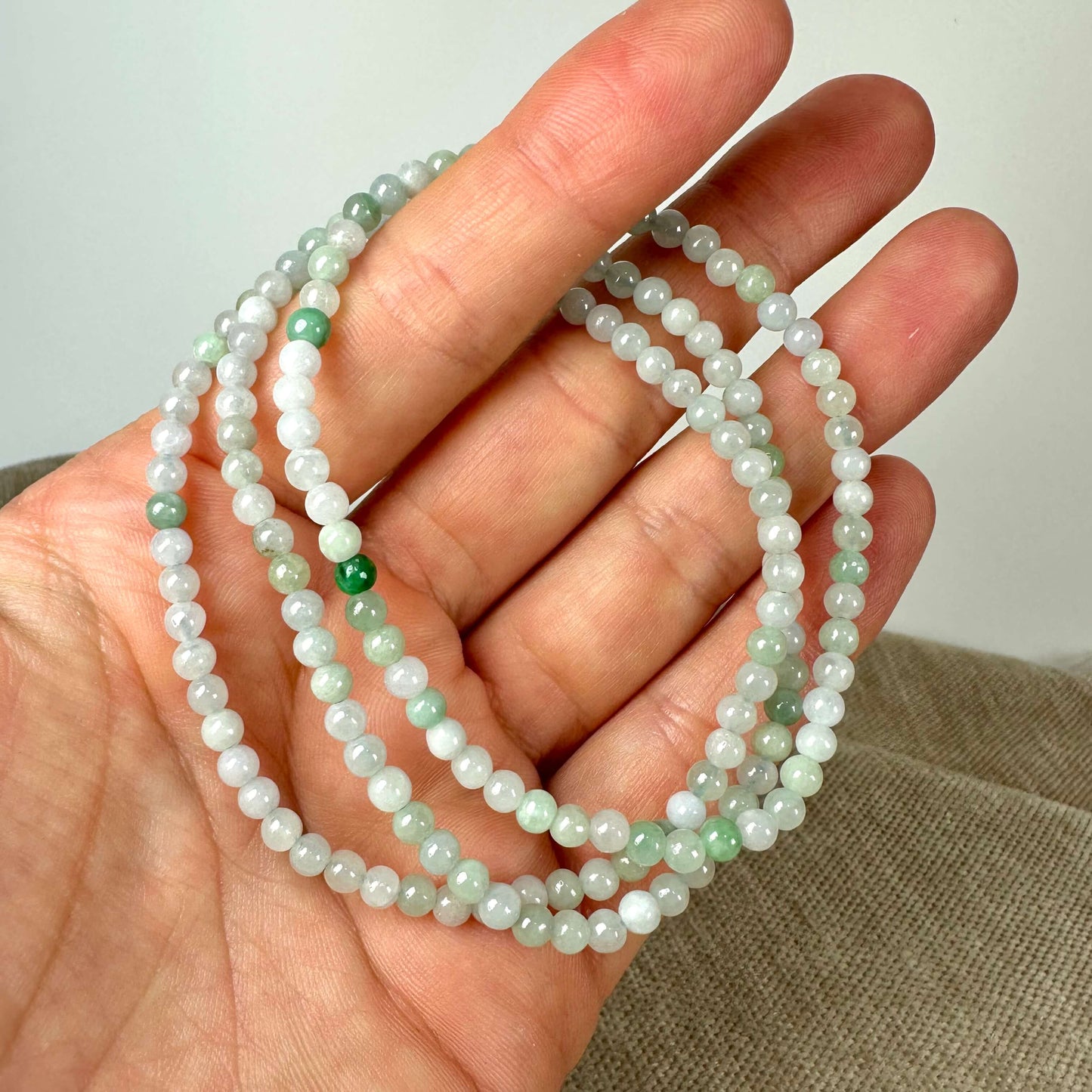 Et armbånd af grønne og hvide perler holdes i en hånd mod en neutral baggrund.