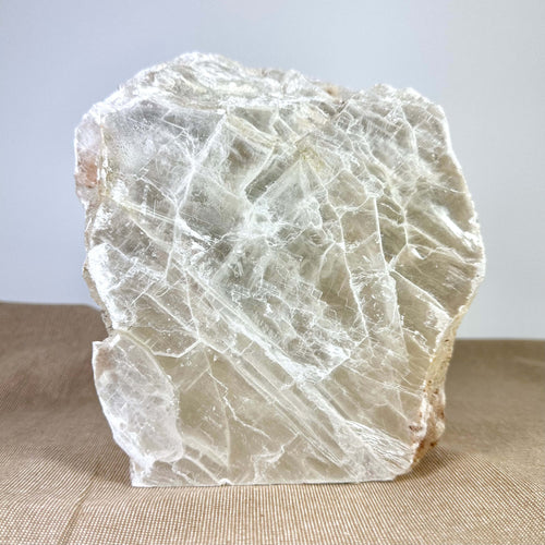 En stor, rå krystal med skarpe linjer og gennemsigtigt udseende, placeret på en brun overflade.