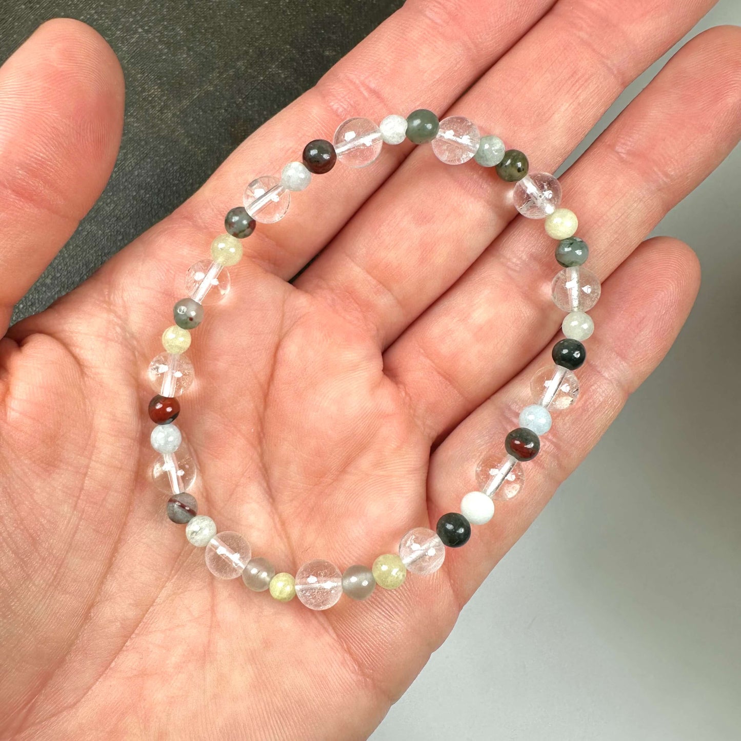 Hånden holder et armbånd med flere-farvede perler, placeret mod en mørk baggrund.