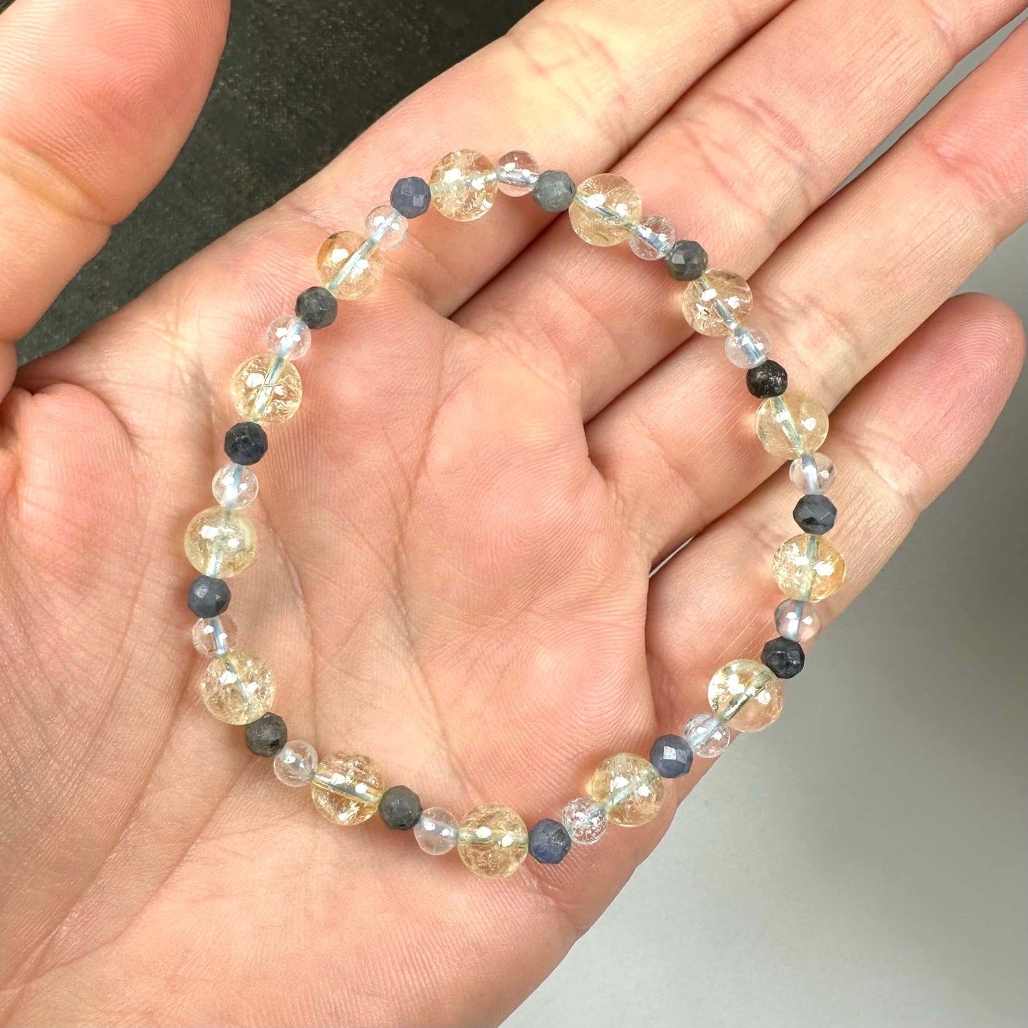 En hånd holder et armbånd med gennemsigtige og sorte perler.