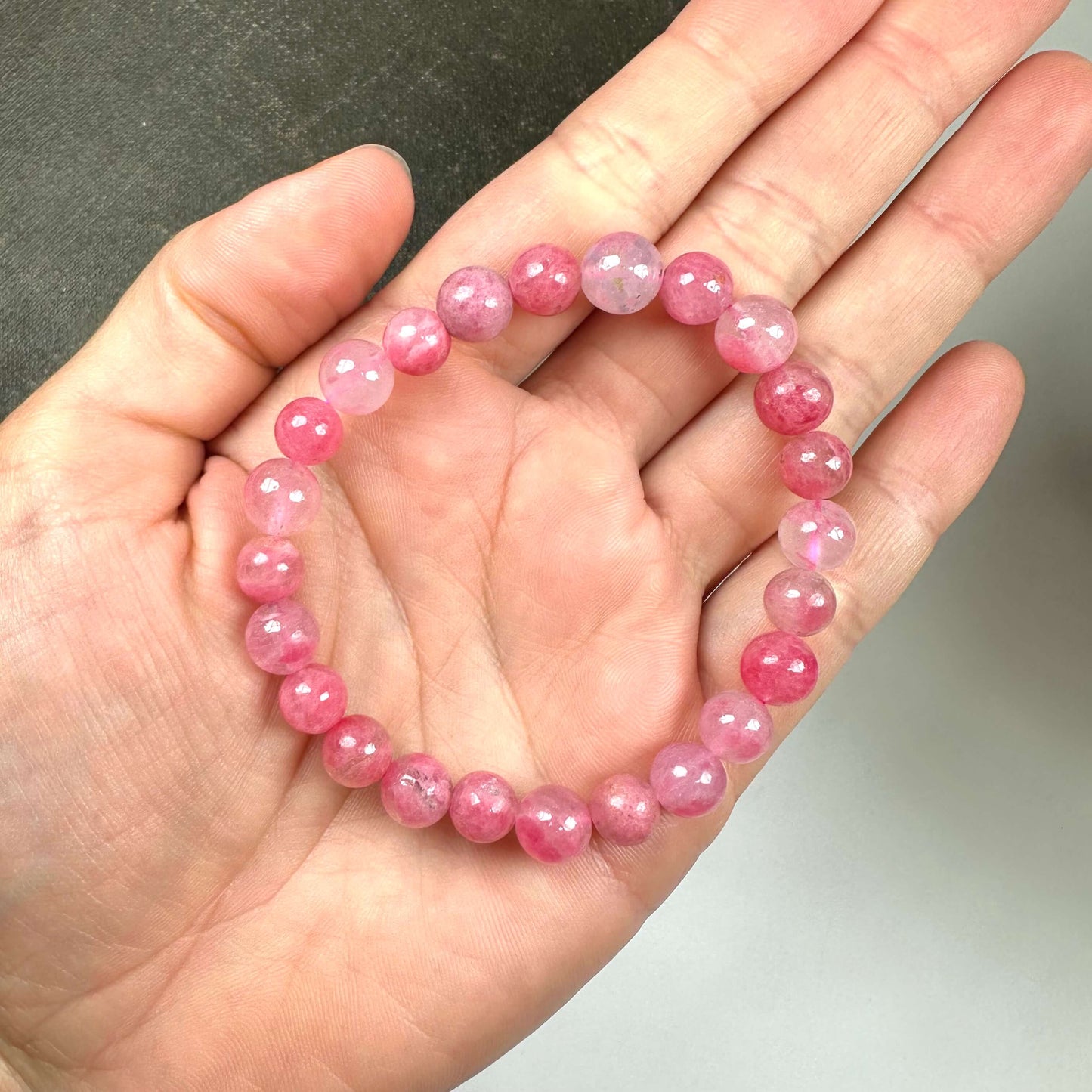 En hånd holder et armbånd lavet af rosa perler på en grå baggrund.