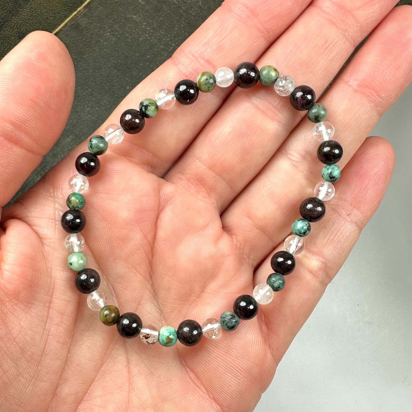 En hånd holder et armbånd med sorte, grønne og gennemsigtige perler.