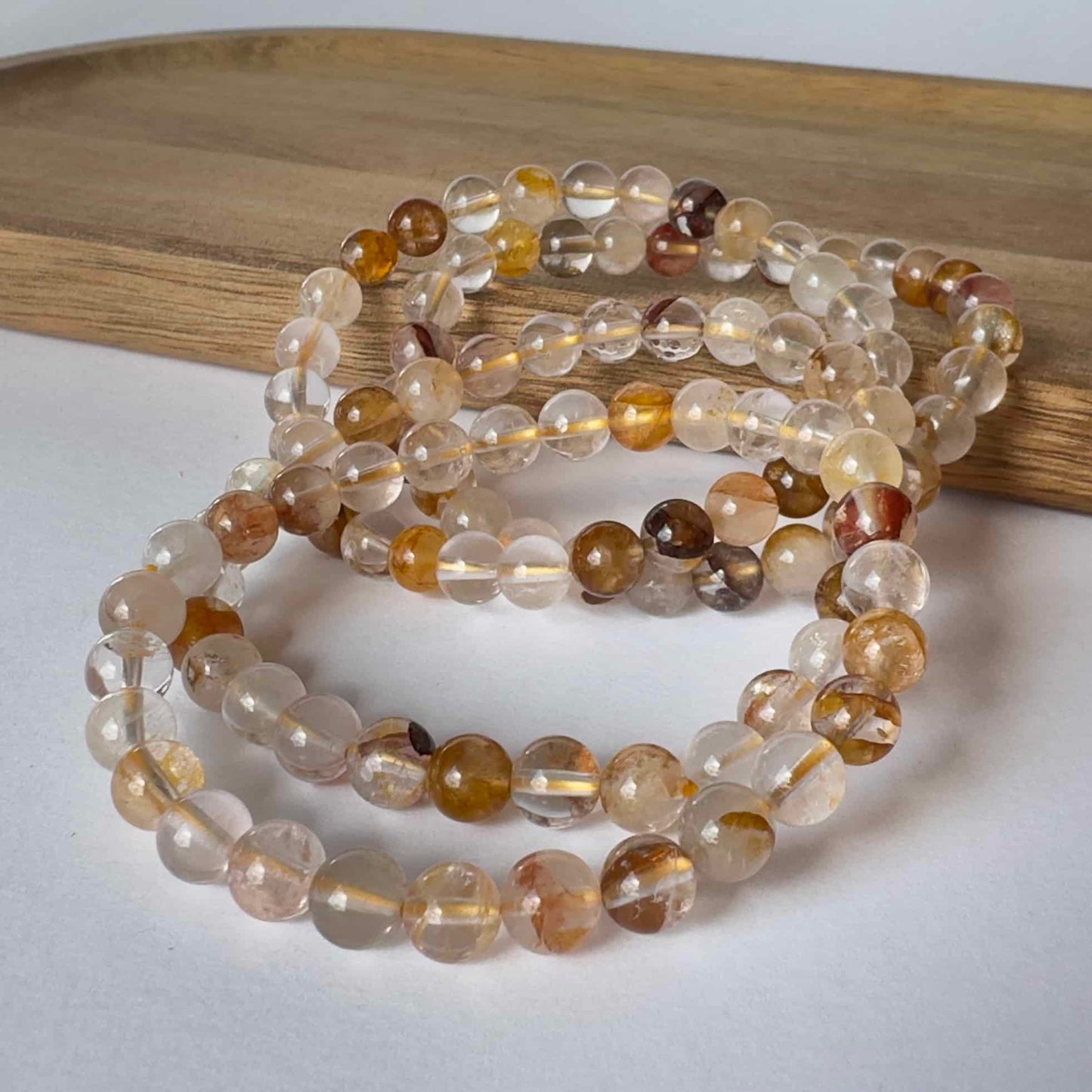 Armbånd lavet af Golden Healer krystalperler, placeret på en træbakke.