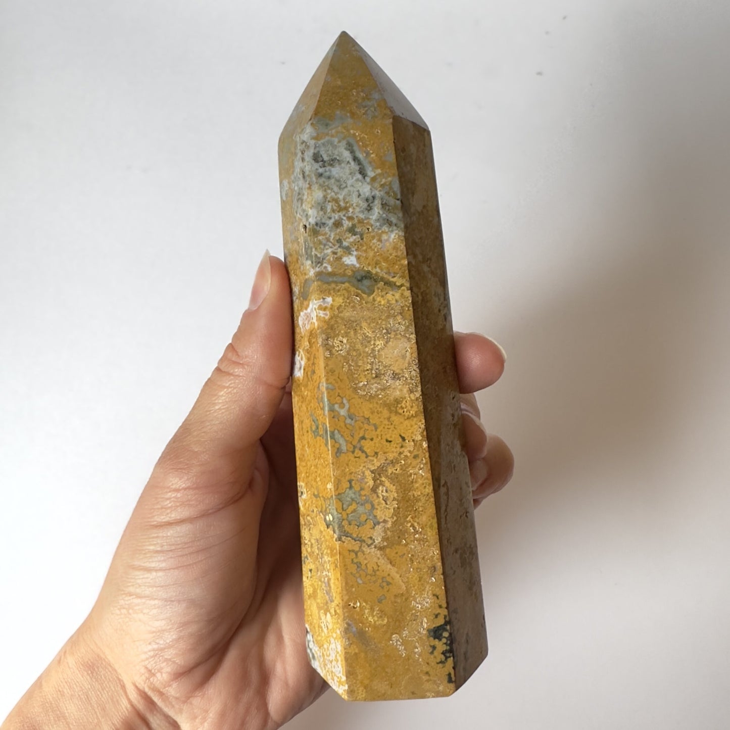 Hånd holder en gul Jaspis Hav tårn krystal mod en hvid baggrund.
