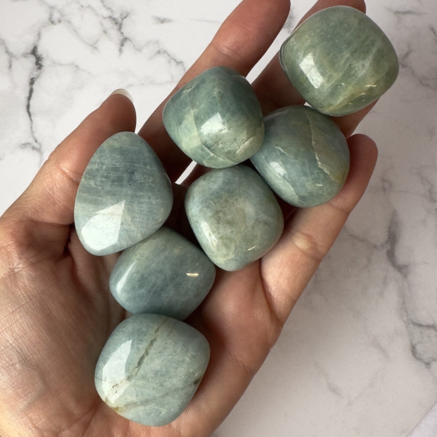 Hånd holder syv polerede akvamarinsten på en lys marmorbaggrund.