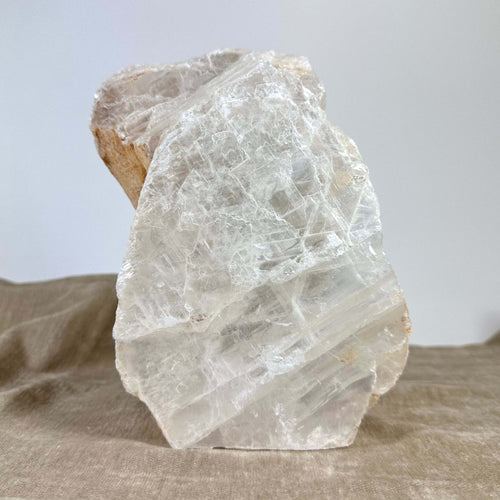 Klar bjergkrystal på en brun klud, tekstur afspejler lys, mod en neutral baggrund.