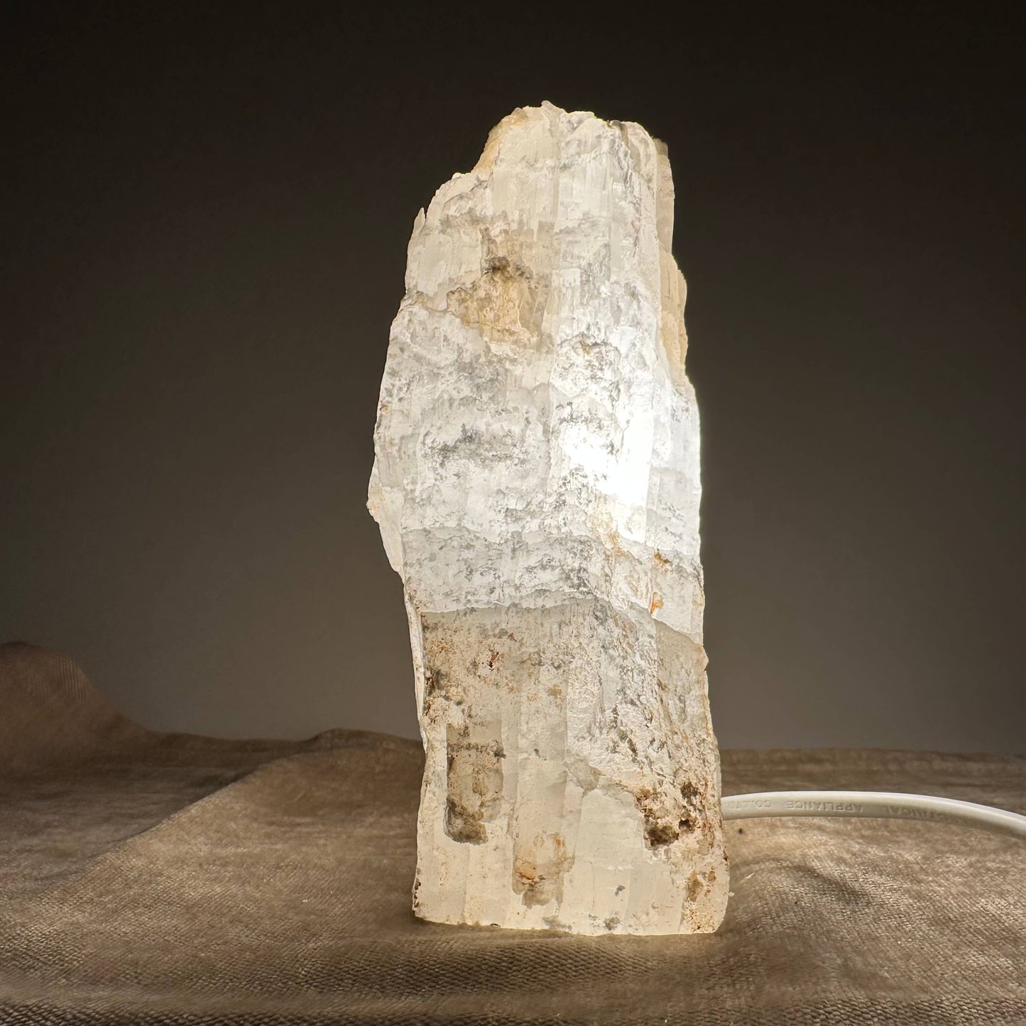 Krystallagtig lampe, der lyser op i et mørkt rum, placeret på en brun overflade.